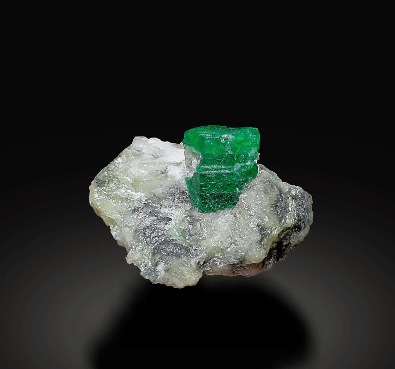 Emerald 桌布 壁紙 — 一顆鮮綠色的祖母綠晶體坐落於粗糙的白色和灰色礦物基質上，背景是純黑色。