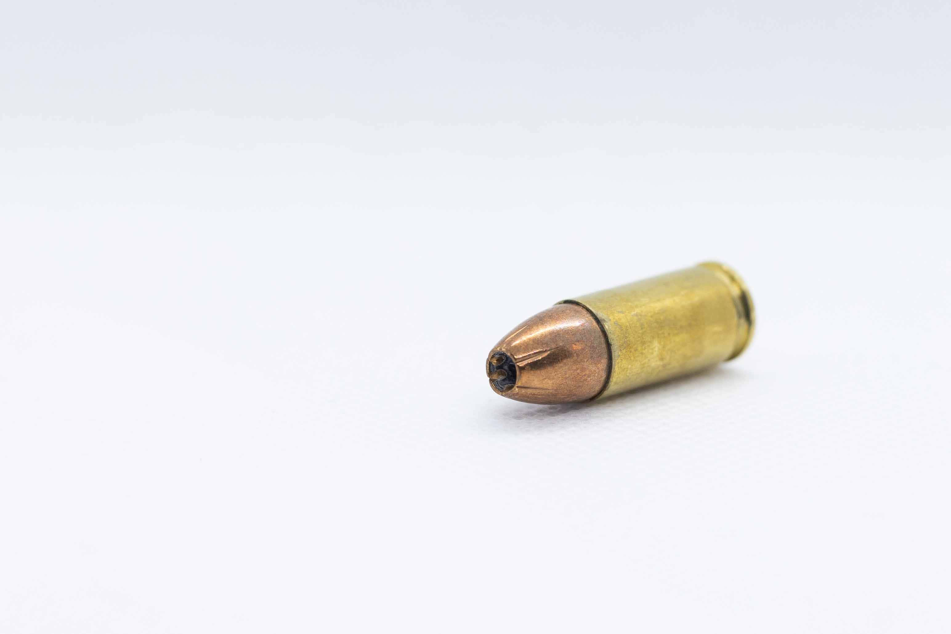 bullet 桌布 壁紙 — 一顆黃銅子彈在明亮的攝影棚燈光下，斜放在純白色表面上。
