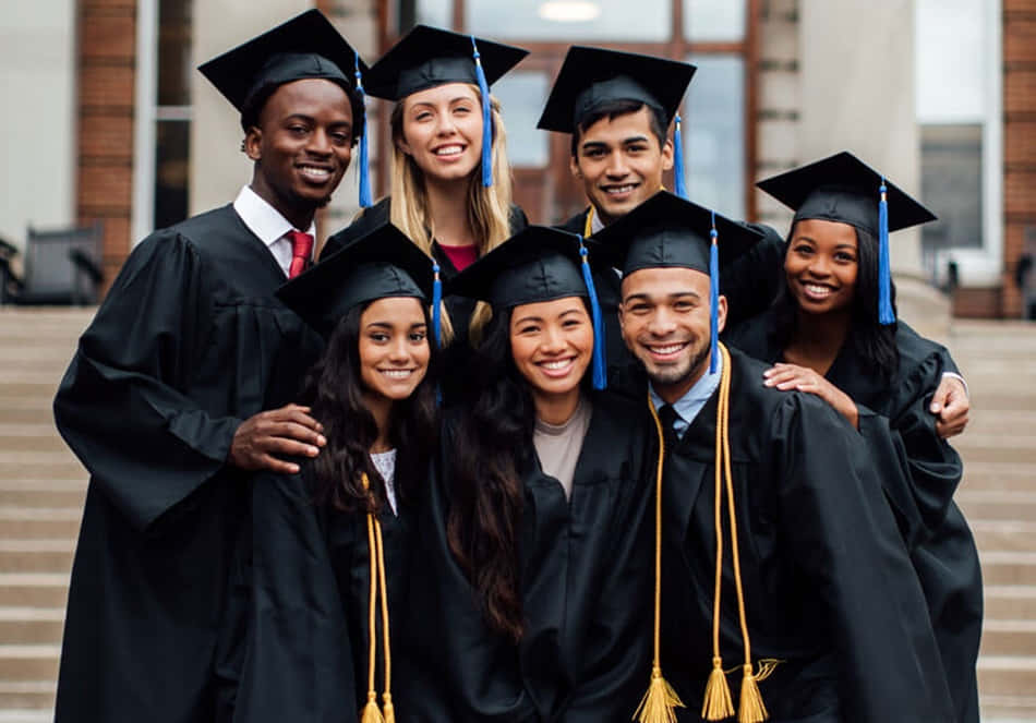 Graduation 桌布 壁紙 — 七位多元化的畢業生身穿黑色學士帽和學士袍，配藍色流蘇，在大學校園戶外燦爛微笑。