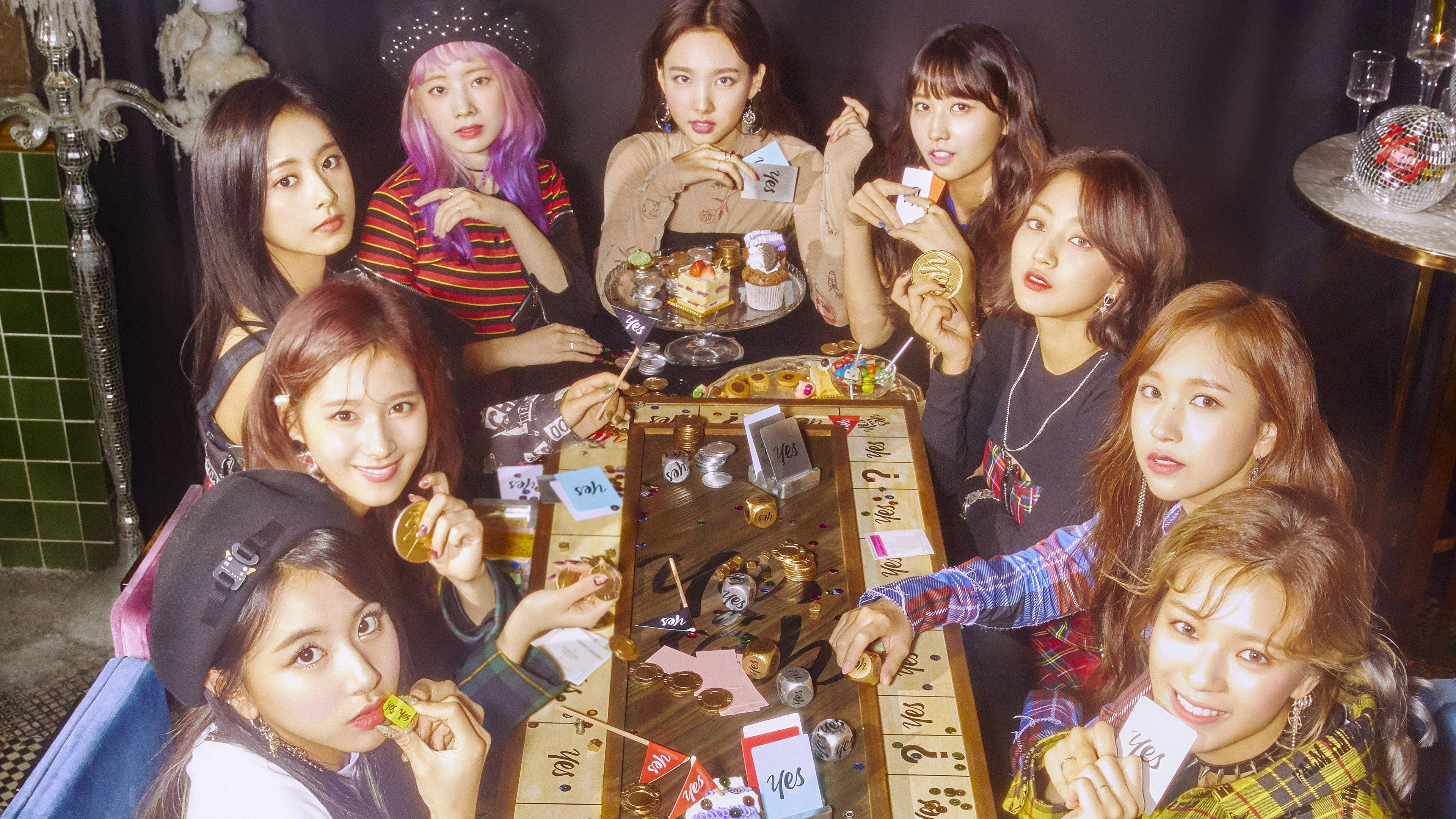 Kpop Aesthetic 桌布 壁紙 — 七位年輕女性穿著時尚服裝，聚集在一張充滿零食和卡片的木桌旁，房間光線昏暗，有綠色瓷磚和迪斯科球。