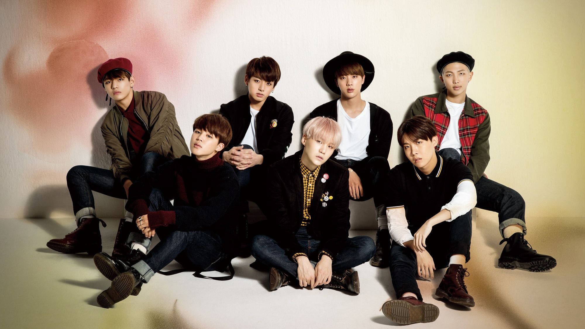 BTS 桌布 壁紙 — 七位年輕男士以時尚休閒裝扮，在柔和的粉紅與米色漸變背景前自信地擺姿勢。