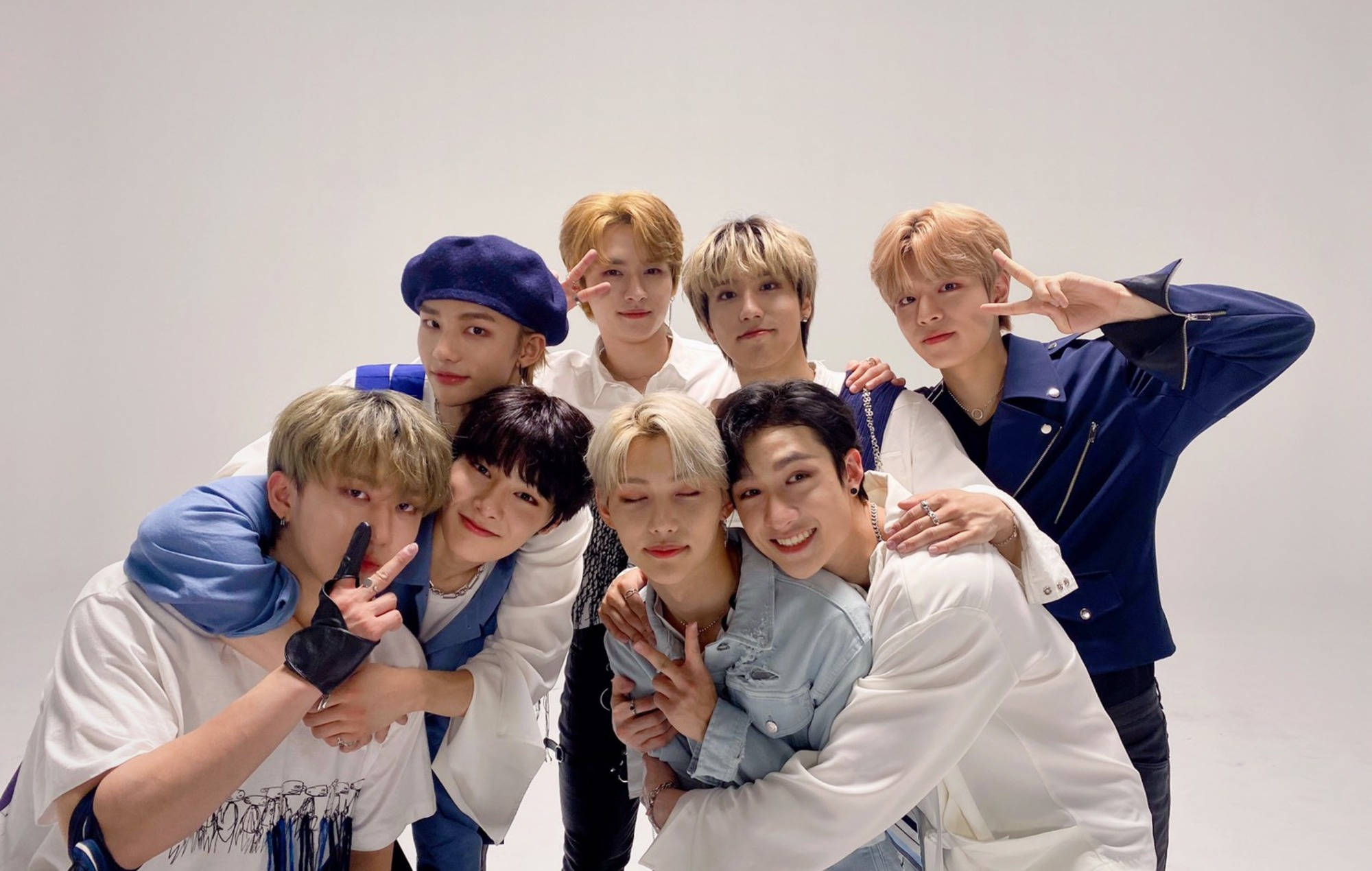 Stray Kids 桌布 壁紙 — 七位年輕男士穿著時尚休閒服裝，在純白背景前緊密地擺姿勢，做出俏皮的手勢。