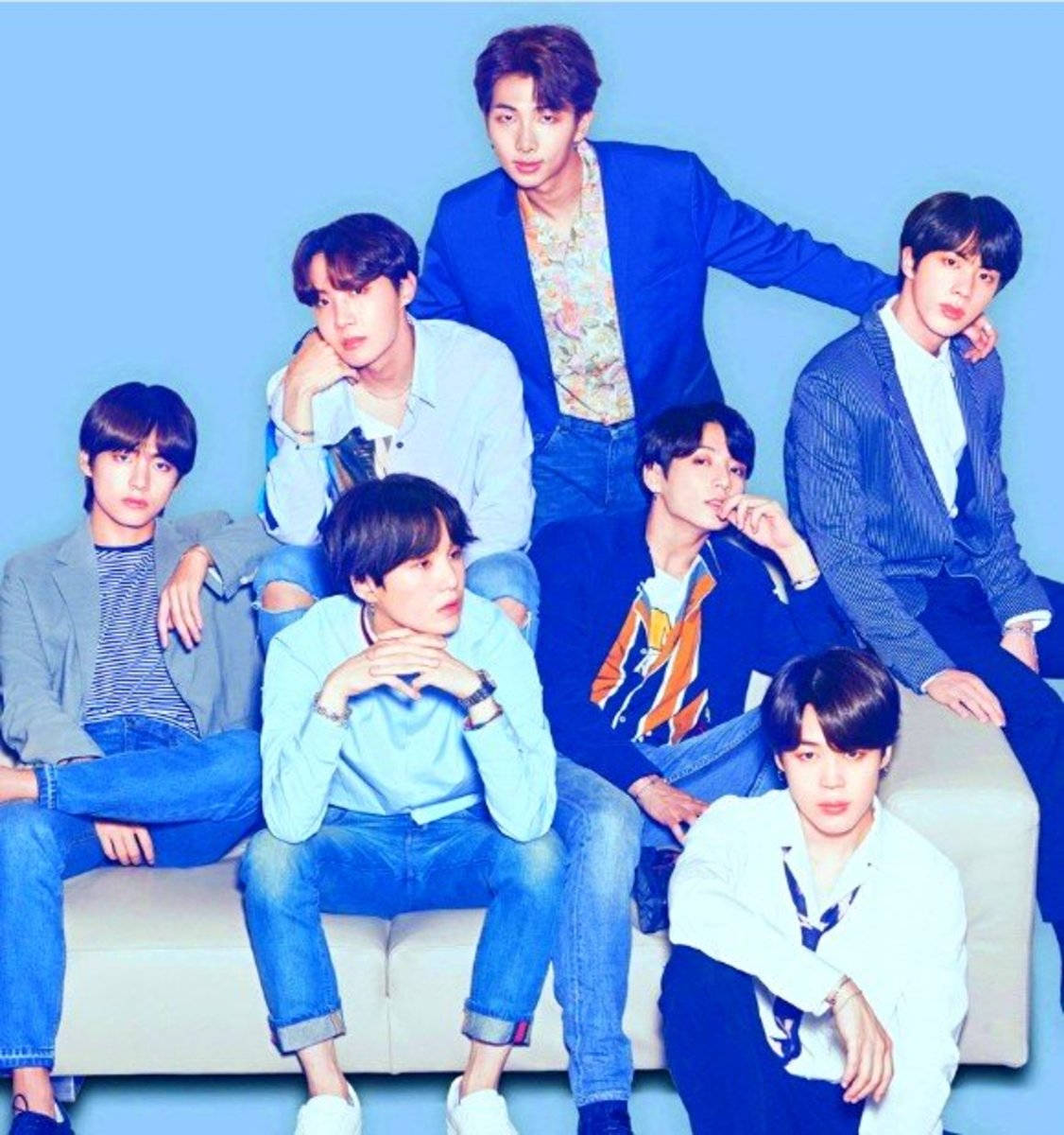 bts photoshoot 桌布 壁紙 — 七位年輕男士穿著時尚休閒服裝，在純藍色背景前的白色沙發上自信地擺姿勢。
