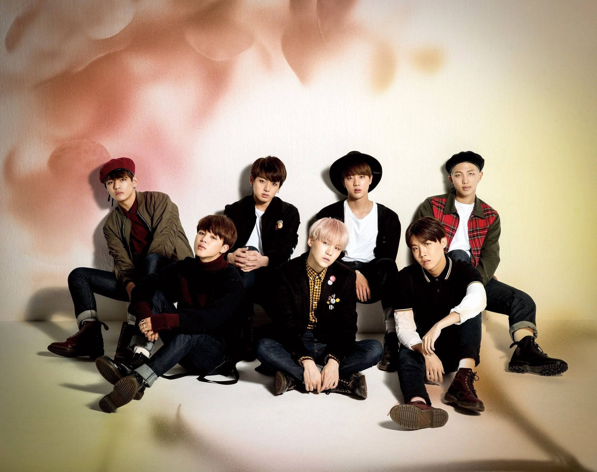 Bigbang 桌布 壁紙 — 七位年輕男士穿著時尚休閒服裝，在柔和的粉紅色和米色漸變背景前自信地擺姿勢。