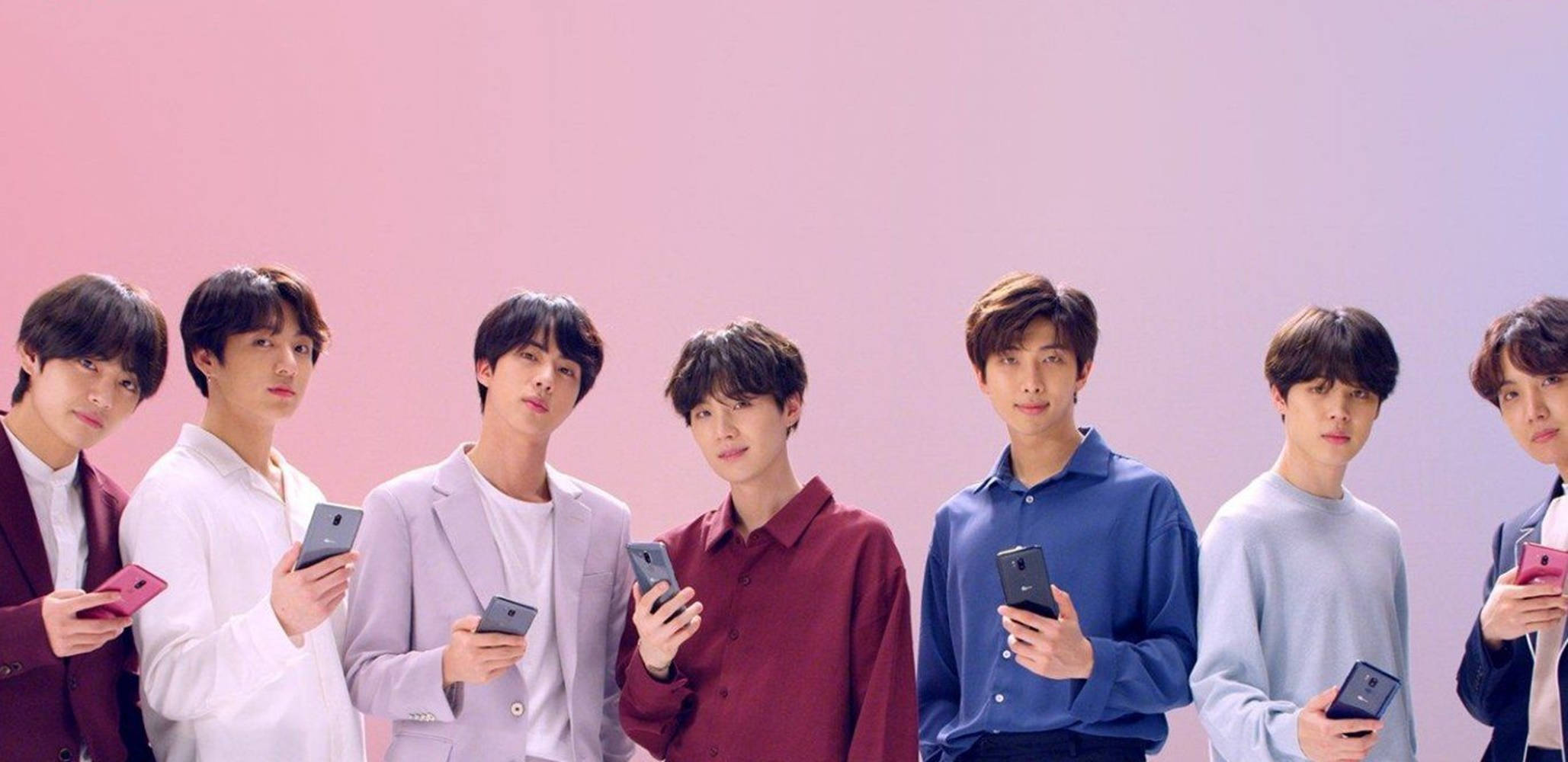 bts 2021 desktop 桌布 壁紙 — 七位年輕男士穿著時尚服裝，在柔和的粉紅色漸變背景前手持智慧型手機。