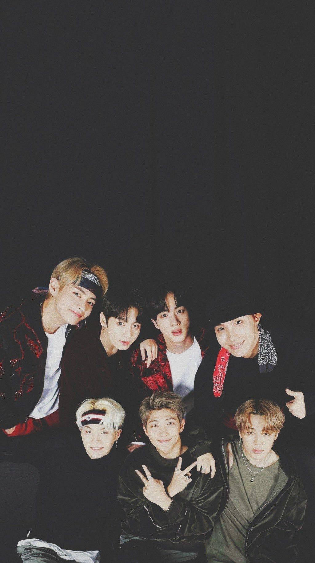 BTS 鎖定螢幕 桌布 壁紙 — 七位年輕男士穿著時尚深色服裝，在黑色背景前緊密擺出俏皮表情。