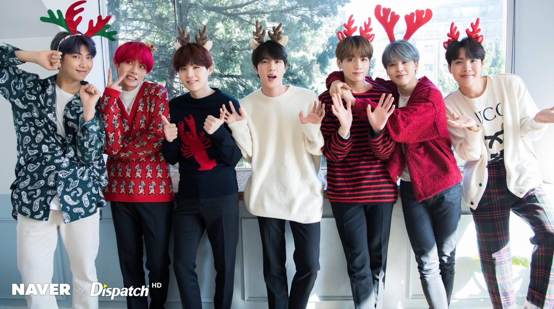 BTS 桌布 壁紙 — 七位年輕男士穿著節日毛衣和馴鹿角，在明亮的窗邊愉快地擺姿勢。