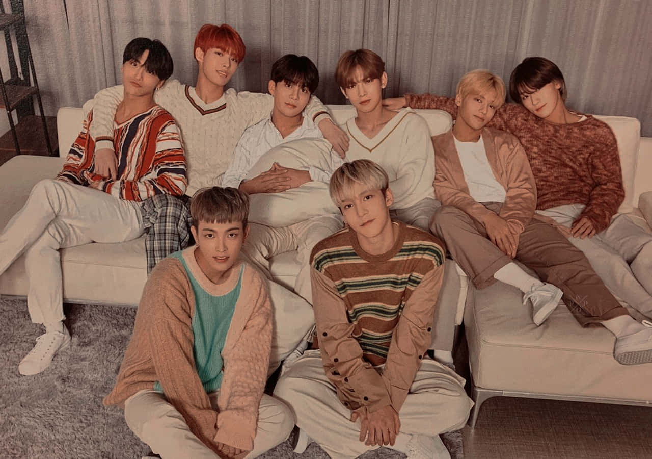 Ateez Desktop 桌布 壁紙 — 七位年輕男士穿著舒適的毛衣，在白色沙發上隨意擺姿勢，背景是柔和的灰色窗簾。