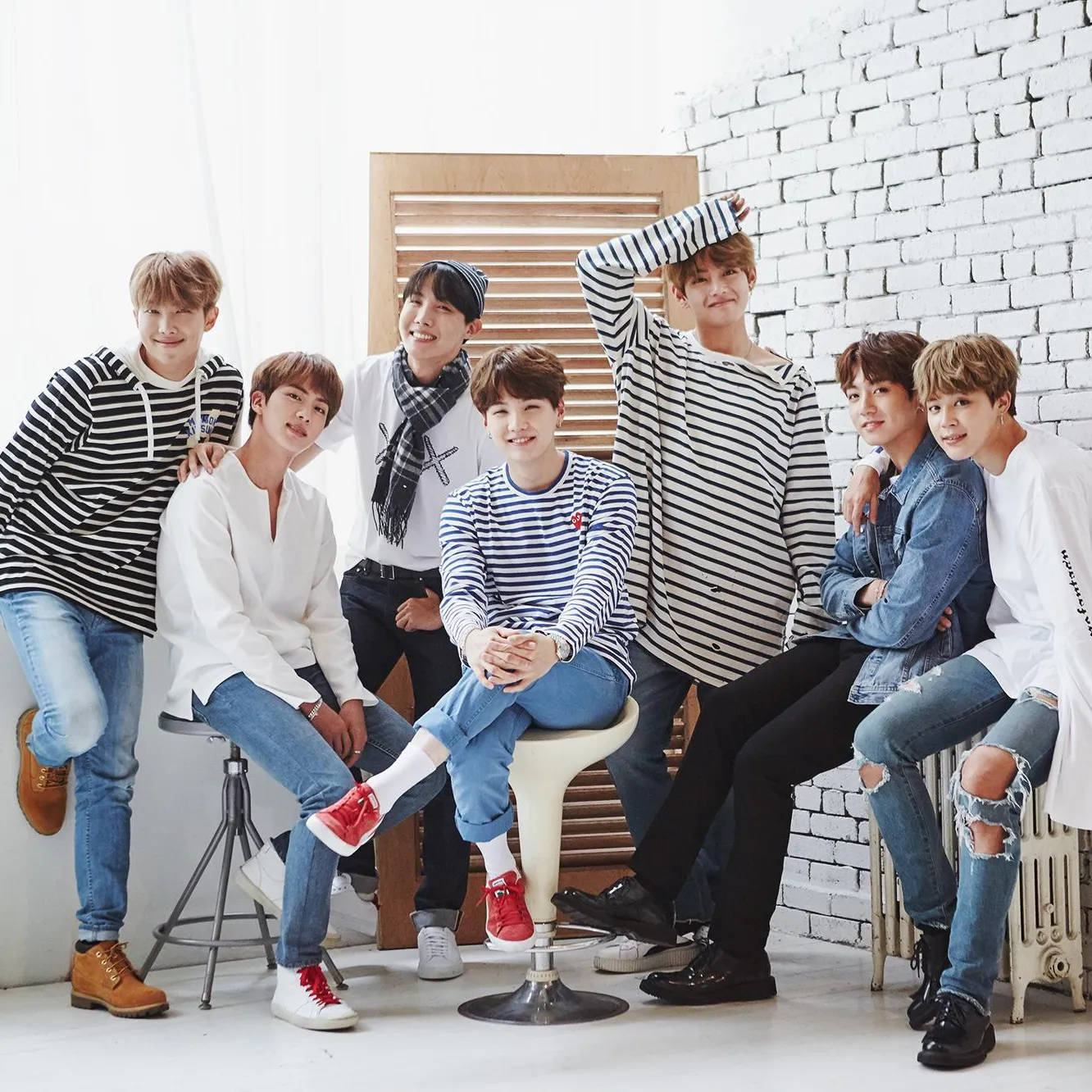BTS 桌布 壁紙 — 七位年輕男士身穿休閒條紋和牛仔服裝，在白色磚牆和木製百葉窗背景前愉快地擺姿勢。