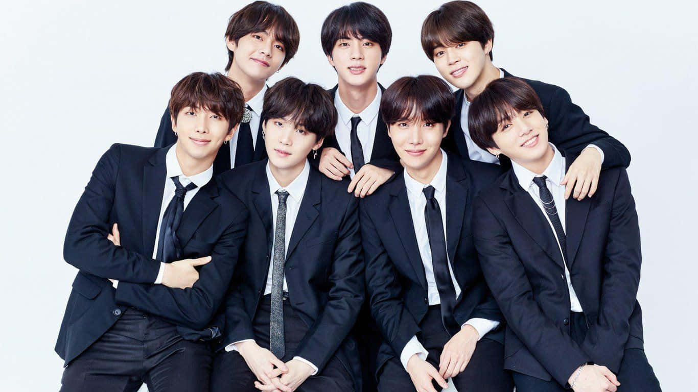 BTS 桌布 壁紙 — 七位年輕男士身穿俐落黑色西裝，在純白背景前自信擺姿勢，帶著溫暖笑容。
