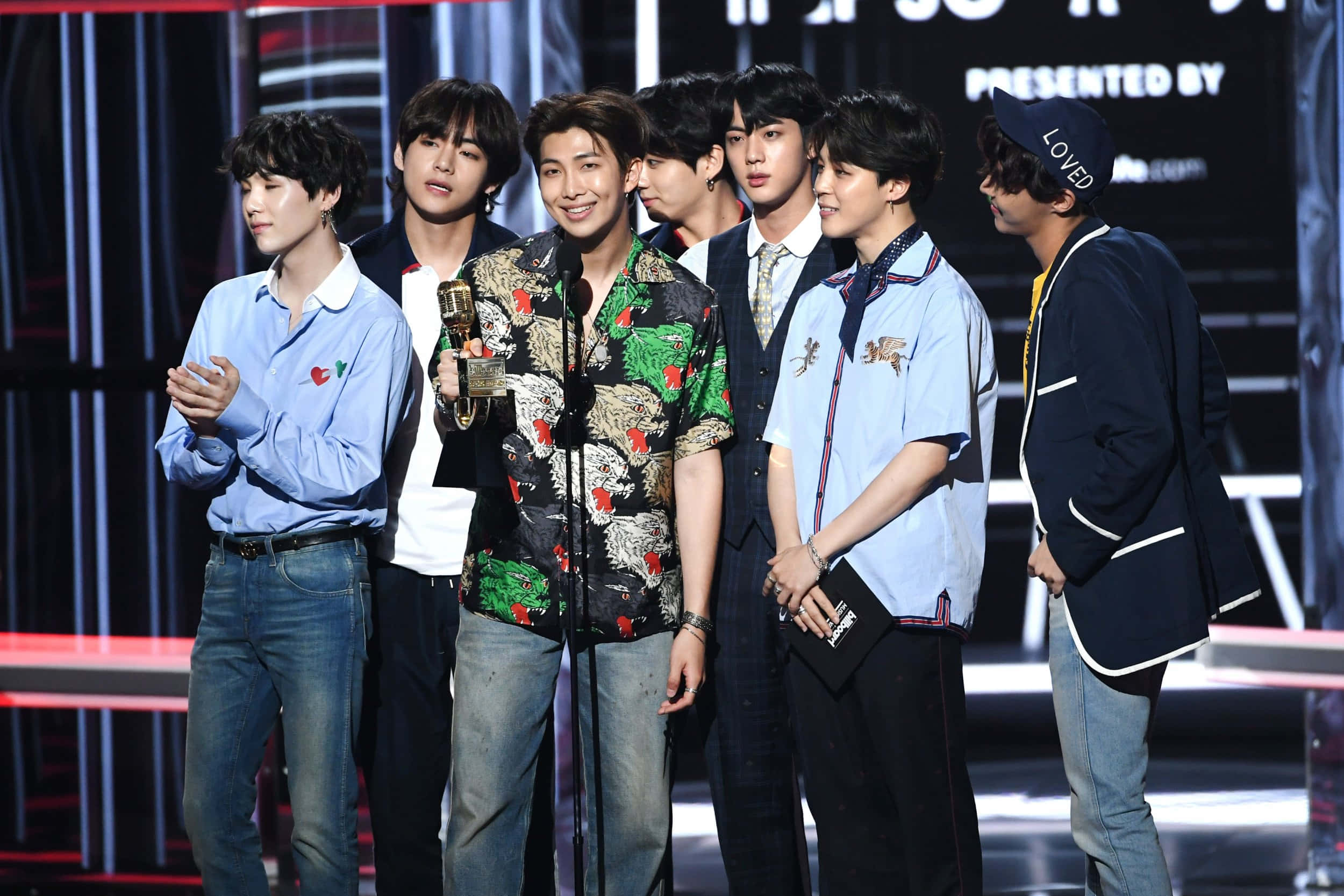 Namjoon 桌布 壁紙 — 七位年輕男士身穿時尚服裝，站在燈光明亮的舞台上，手持獎項並對著鏡頭微笑。