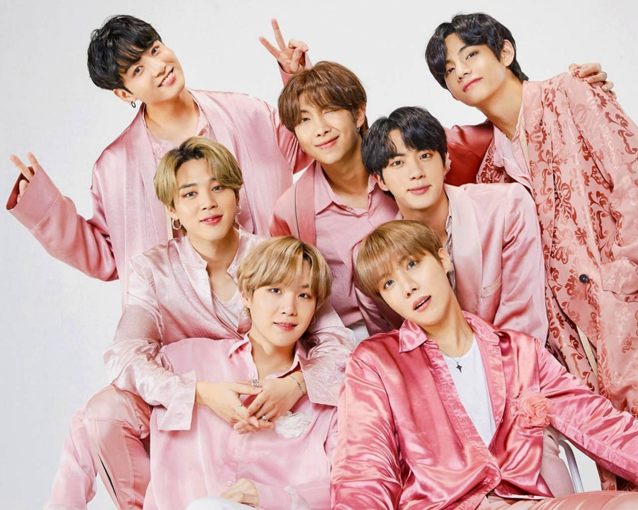 BTS 桌布 桌布 壁紙 — 七位年輕男士身穿閃亮粉紅色服裝，在純白色背景前以俏皮手勢愉快地擺姿勢。