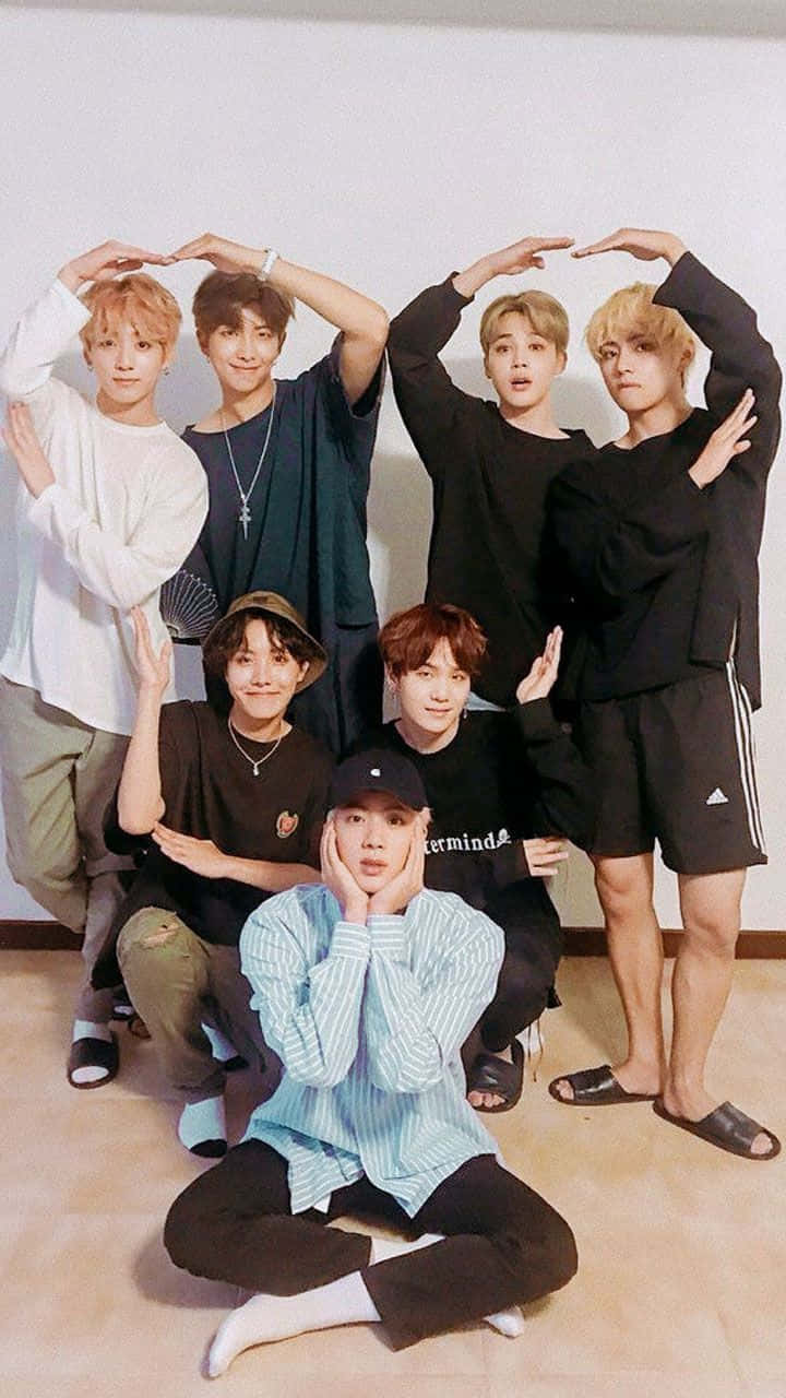 BTS 桌布 壁紙 — 七位年輕男子在室內俏皮地擺姿勢，雙手在頭頂比出心形。