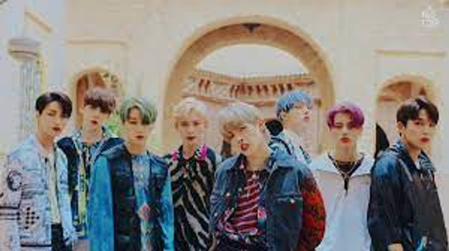 Ateez Desktop 桌布 壁紙 — 七位年輕男子擁有色彩繽紛的頭髮，自信地站在陽光普照的庭院中的石拱門下。
