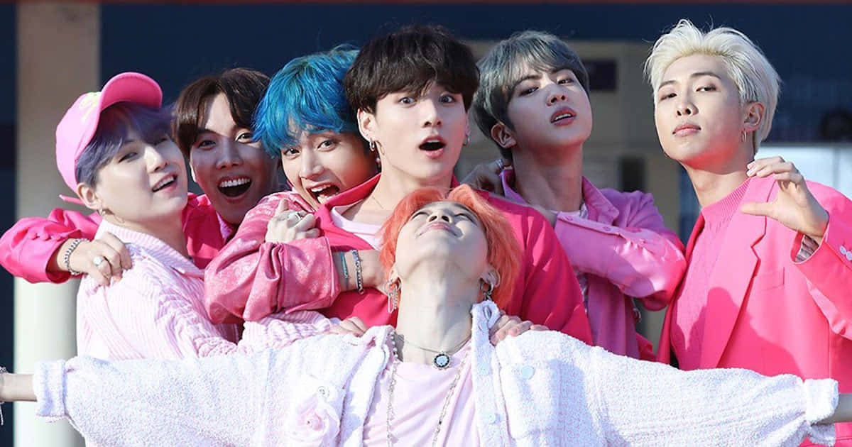 BTS 桌布 壁紙 — 七位年輕男子擁有鮮豔的髮色和粉紅色服裝，在明亮的日光下充滿活力地在戶外擺姿勢。