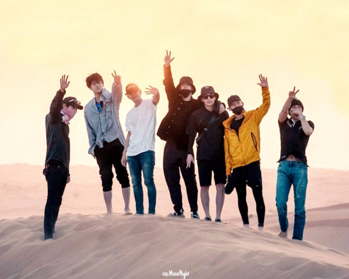 Exo Desktop 桌布 壁紙 — 七位年輕男子穿著休閒服裝，在沙丘上愉快地擺姿勢，背後是溫暖的金色日落光線。