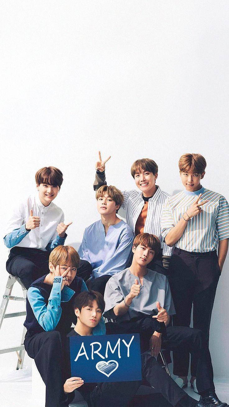 BTS 2021 桌布 壁紙 — 七位年輕男子身穿休閒服裝，在純白背景前開心地擺姿勢，其中一人手持藍色標語牌，上面寫著ARMY。