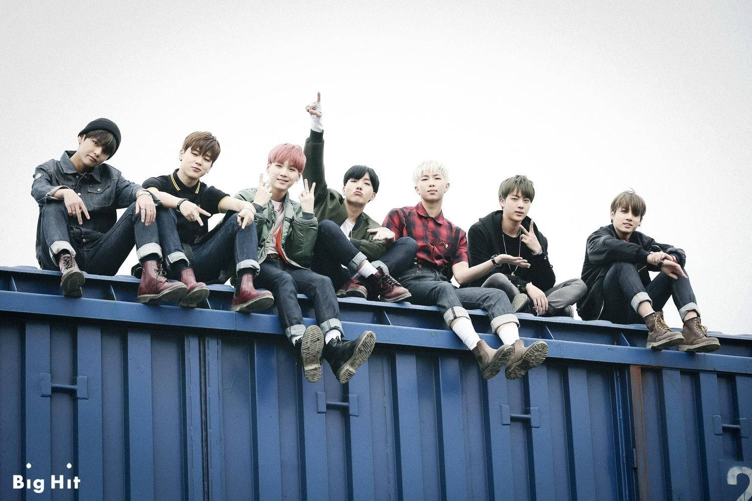 BTS 桌布 壁紙 — 七位年輕男子身穿休閒街頭服飾，自信地站在藍色貨櫃上，背景是淡色天空。