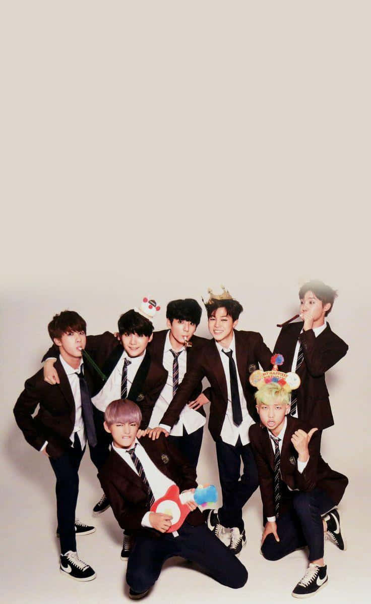 BTS 桌布 壁紙 — 七位年輕男子身穿相配的校服，在純米色背景前用色彩繽紛的道具俏皮地擺姿勢。