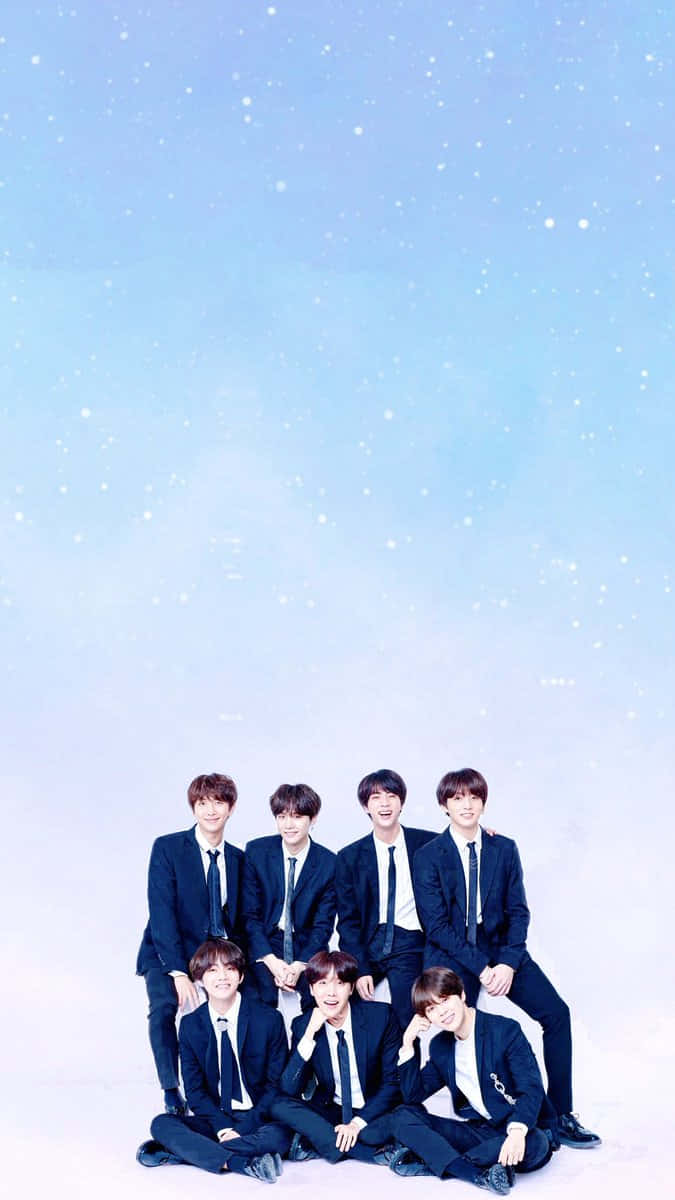 BTS 桌布 壁紙 — 七位年輕男子身穿相配的深色西裝，在飄著雪花的柔和藍天下愉快地擺姿勢。