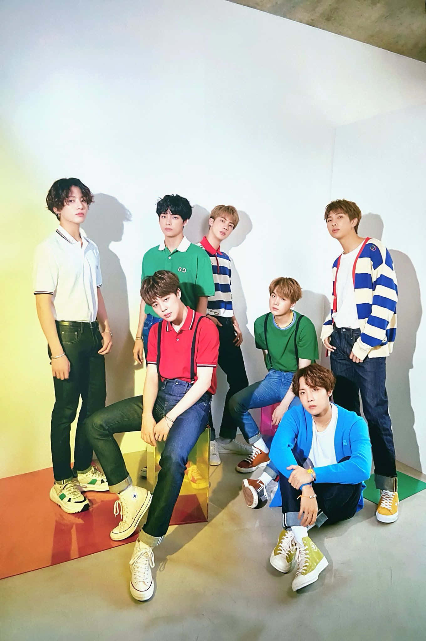 BTS 桌布 壁紙 — 七位年輕男子身穿色彩繽紛的休閒服裝，在純白牆壁和鮮豔地板裝飾前自信地擺姿勢。