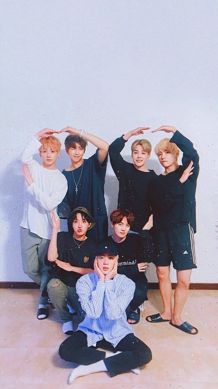 BTS 鎖定螢幕 桌布 壁紙 — 七位年輕男性在一個光線柔和、色調粉彩的簡約房間裡擺出俏皮的姿勢。