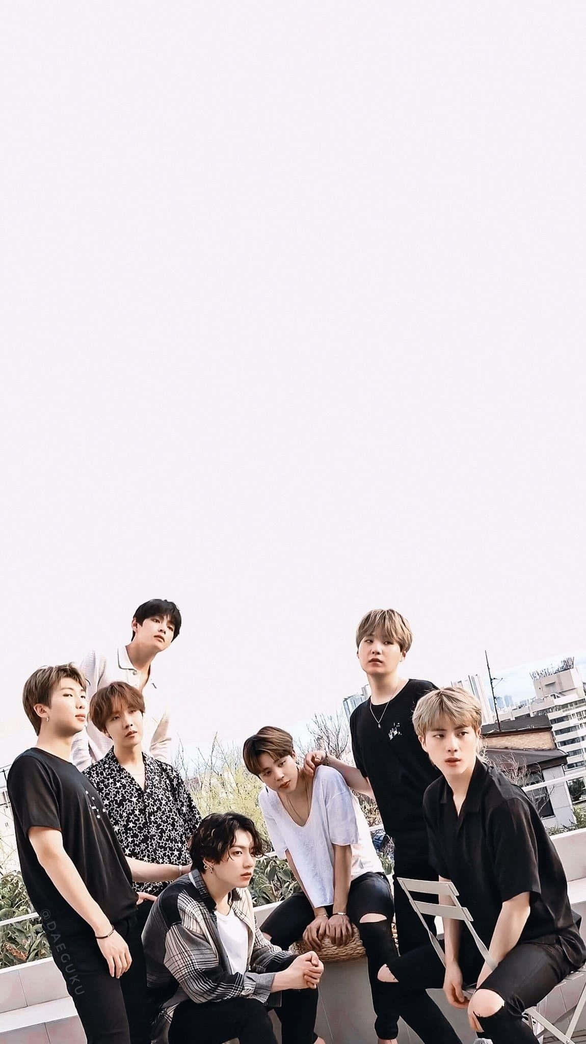 BTS 桌布 壁紙 — 七位年輕男性穿著休閒街頭服飾，在屋頂上自信地擺姿勢，背景是明亮的陰天和城市建築。