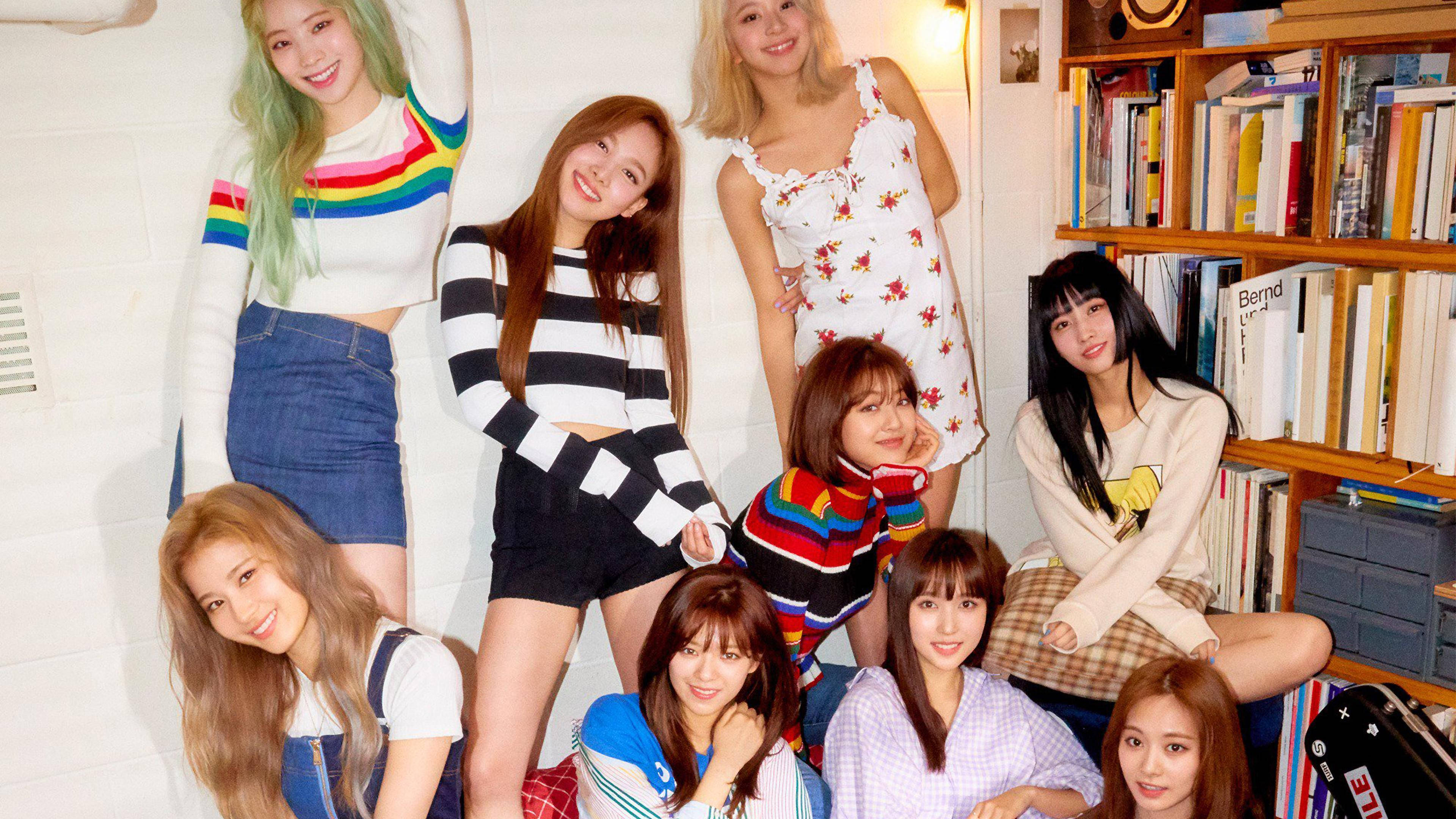 Kpop Aesthetic 桌布 壁紙 — 七位微笑的年輕女性穿著色彩繽紛的休閒服裝，在一個有書架和溫暖照明的舒適房間裡愉快地擺姿勢。