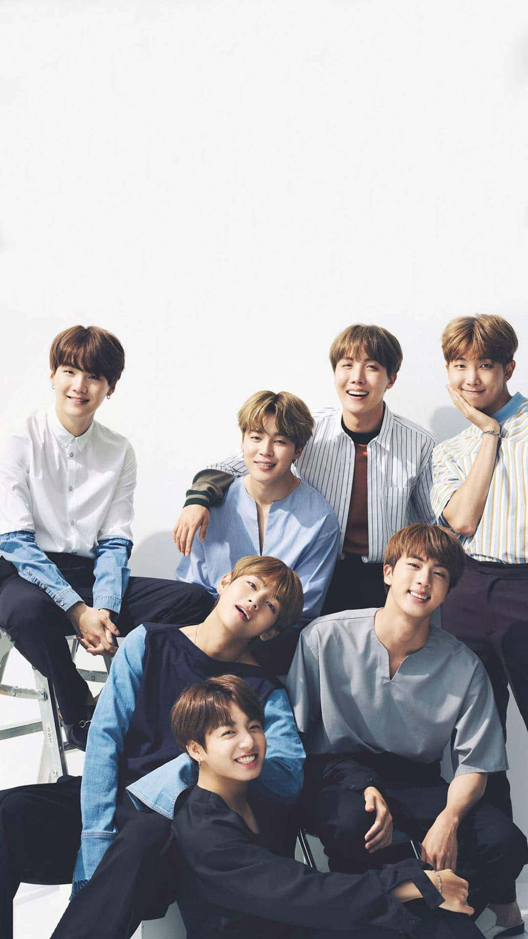 BTS 桌布 壁紙 — 七位微笑的年輕男士穿著休閒襯衫，在明亮的白色攝影棚背景前一起擺姿勢。