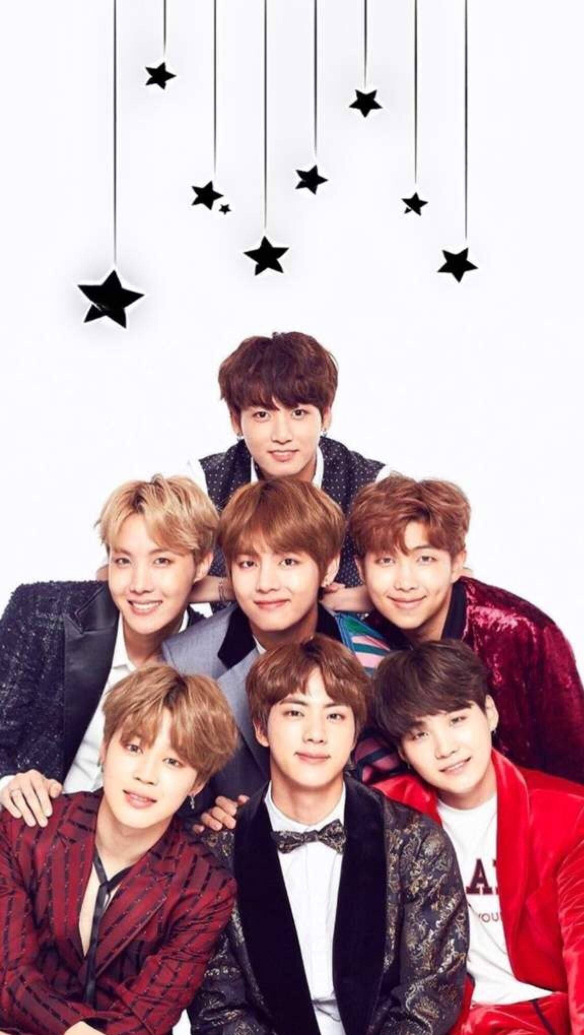 BTS 鎖定螢幕 桌布 壁紙 — 七位微笑的年輕男士穿著時尚天鵝絨和圖案西裝，在白色背景懸掛的黑色星星下一起擺姿勢。