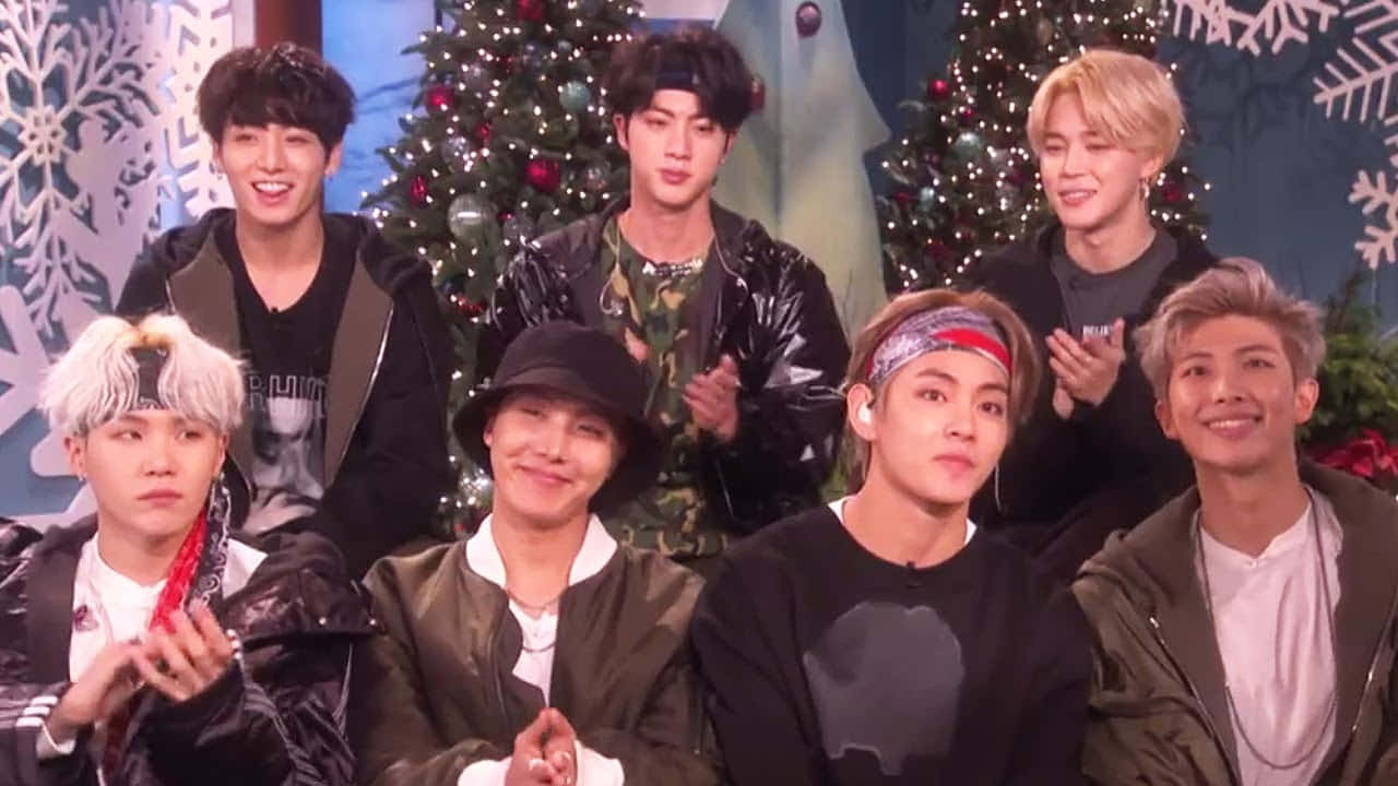 七位K-pop偶像在聖誕樹和雪花裝飾前微笑。 — 防彈少年團 合照 壁紙