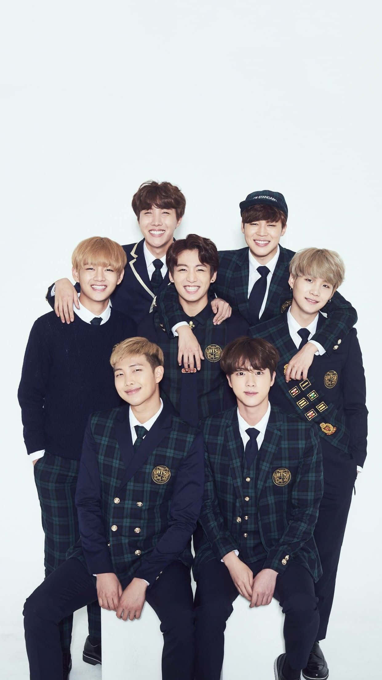 BTS 桌布 壁紙 — 七位微笑的年輕男士穿著相配的深色格子西裝外套，在純白背景前一起擺姿勢。
