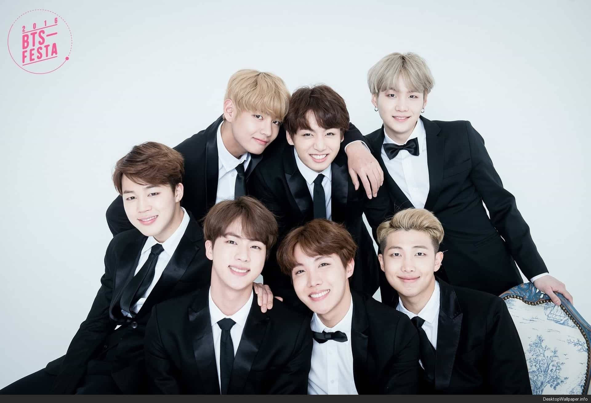 BTS 桌布 壁紙 — 七位微笑的年輕男士身穿黑色禮服，在純白攝影棚背景前緊密地擺姿勢。