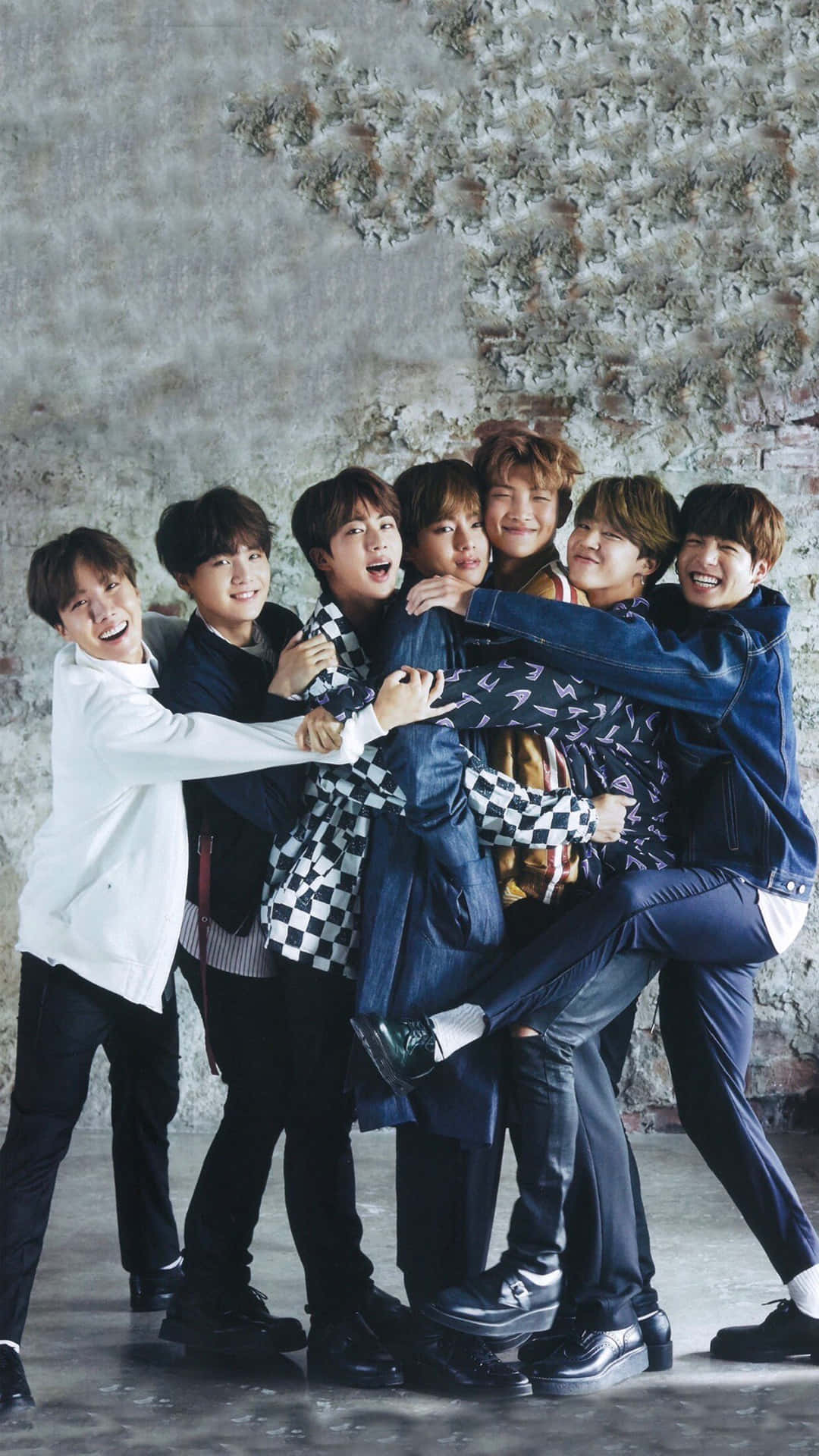 Bts Funny 桌布 壁紙 — 七位微笑的年輕男子穿著休閒服裝，在紋理混凝土牆前一起俏皮地擺姿勢。