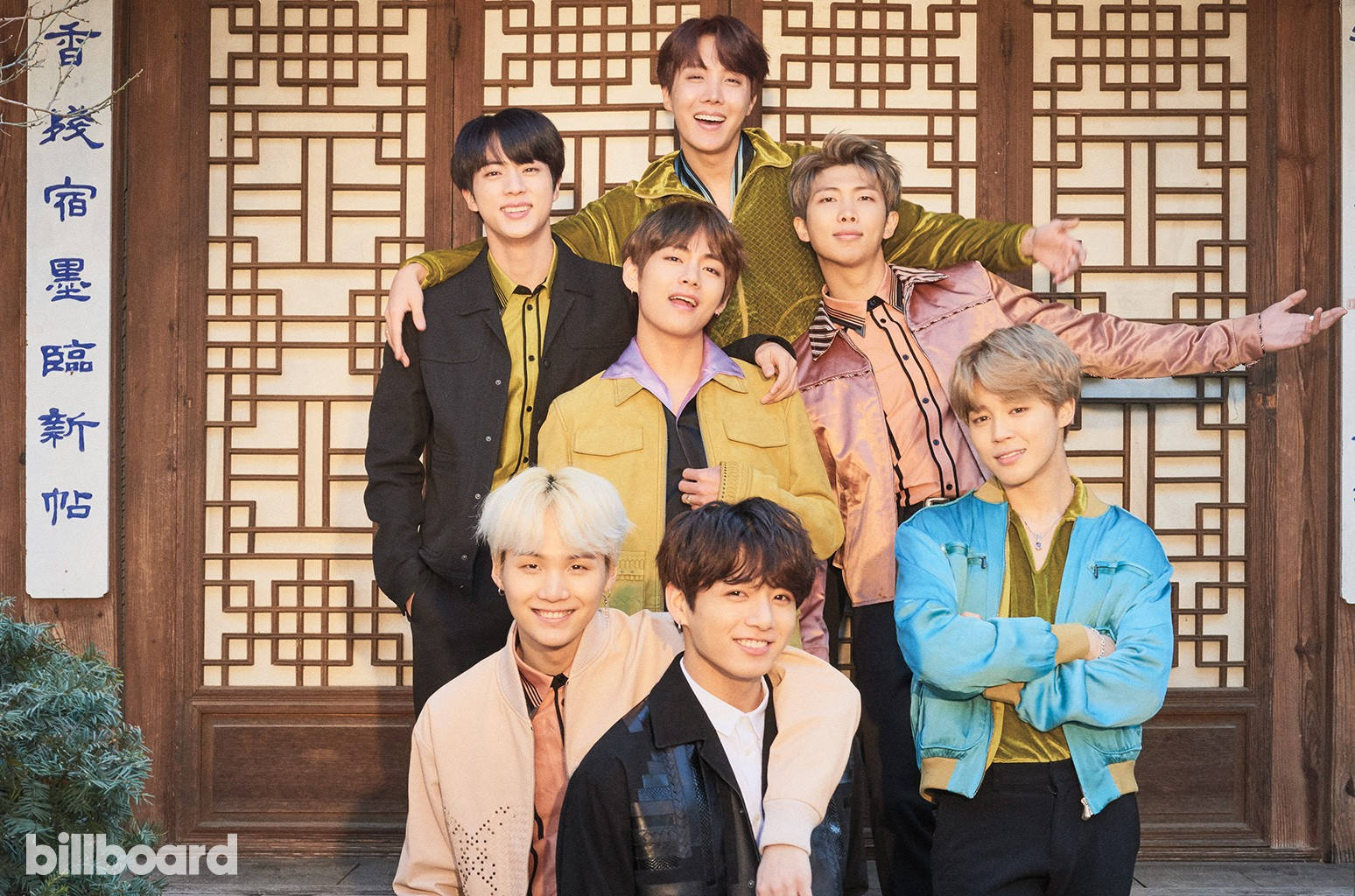 BTS 2021 桌布 壁紙 — 七位微笑的年輕男子身穿色彩繽紛的夾克，在帶有中文字的傳統木格門前愉快地擺姿勢。