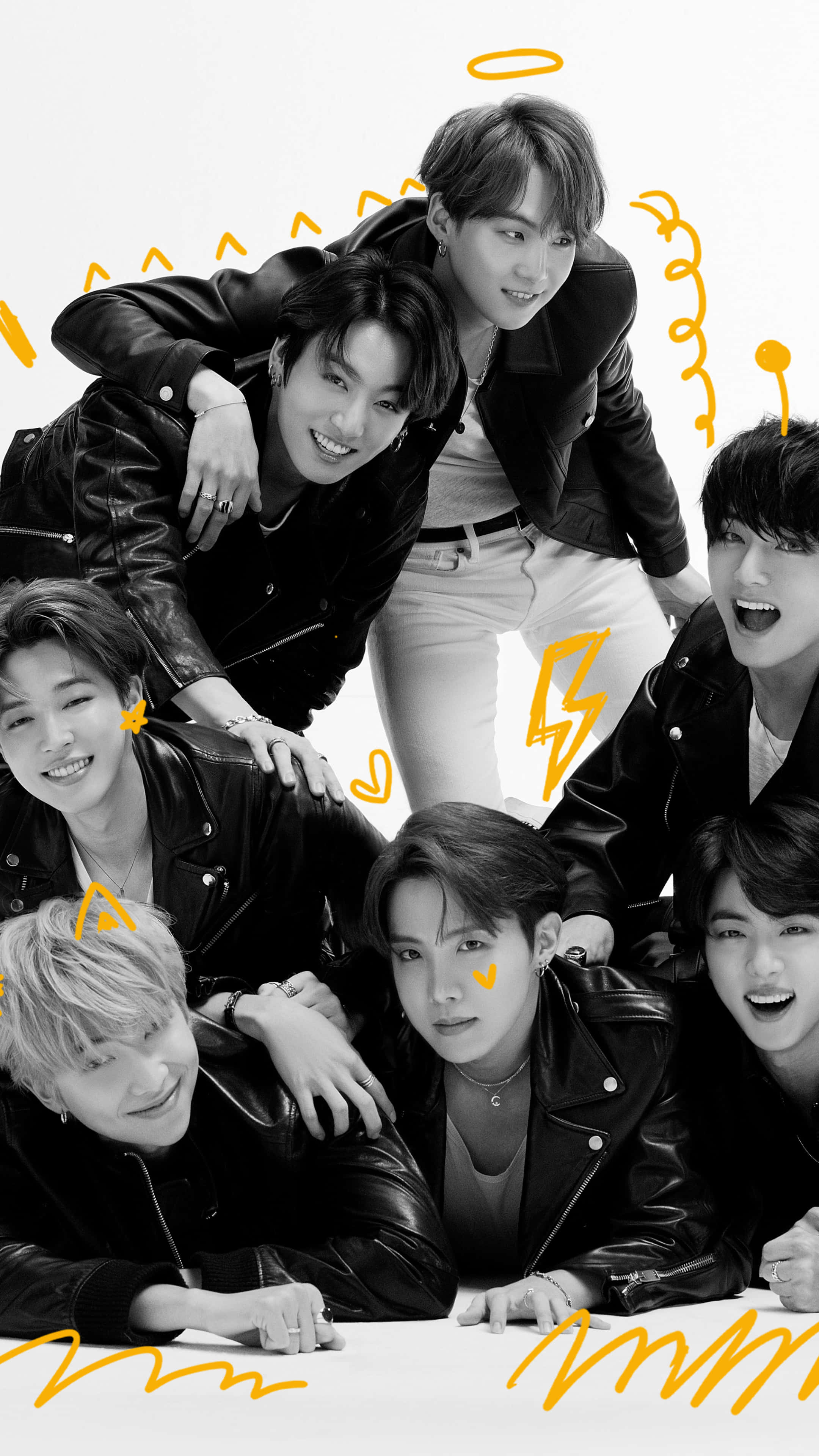 BTS 桌布 壁紙 — 七位微笑的年輕男子身穿黑色皮夾克，在帶有黃色塗鴉點綴的白色背景前俏皮地擺姿勢。