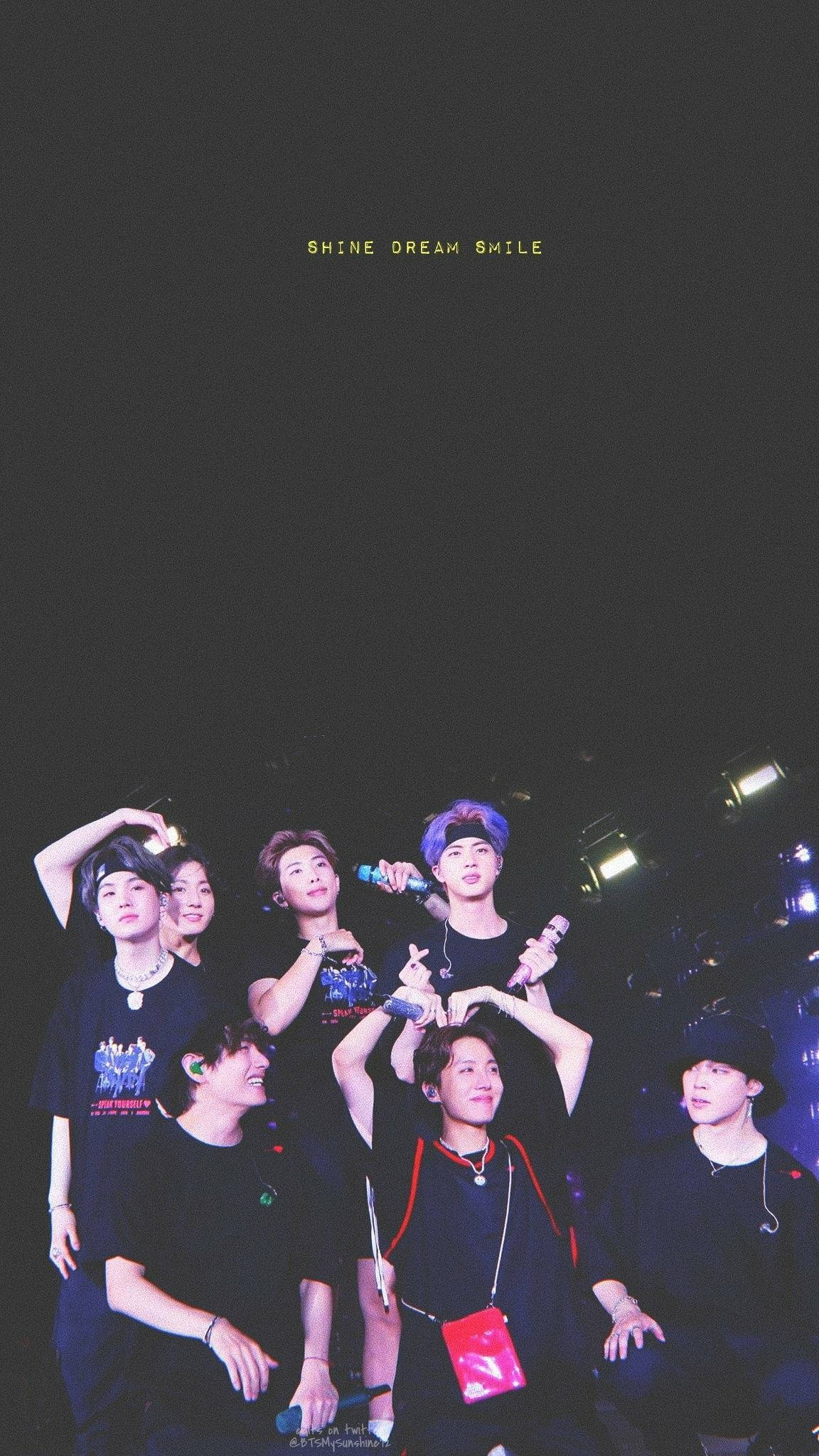 BTS 桌布 壁紙 — 七位微笑的表演者身穿黑色服裝，在舞台燈光下一同擺姿勢，上方有「SHINE DREAM SMILE」字樣。