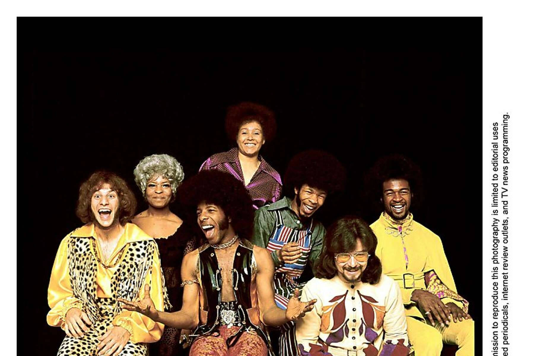band 桌布 壁紙 — 七位快樂的1970年代音樂家，留著非洲式髮型，穿著大膽圖案的服裝，在黑色背景前擺姿勢。