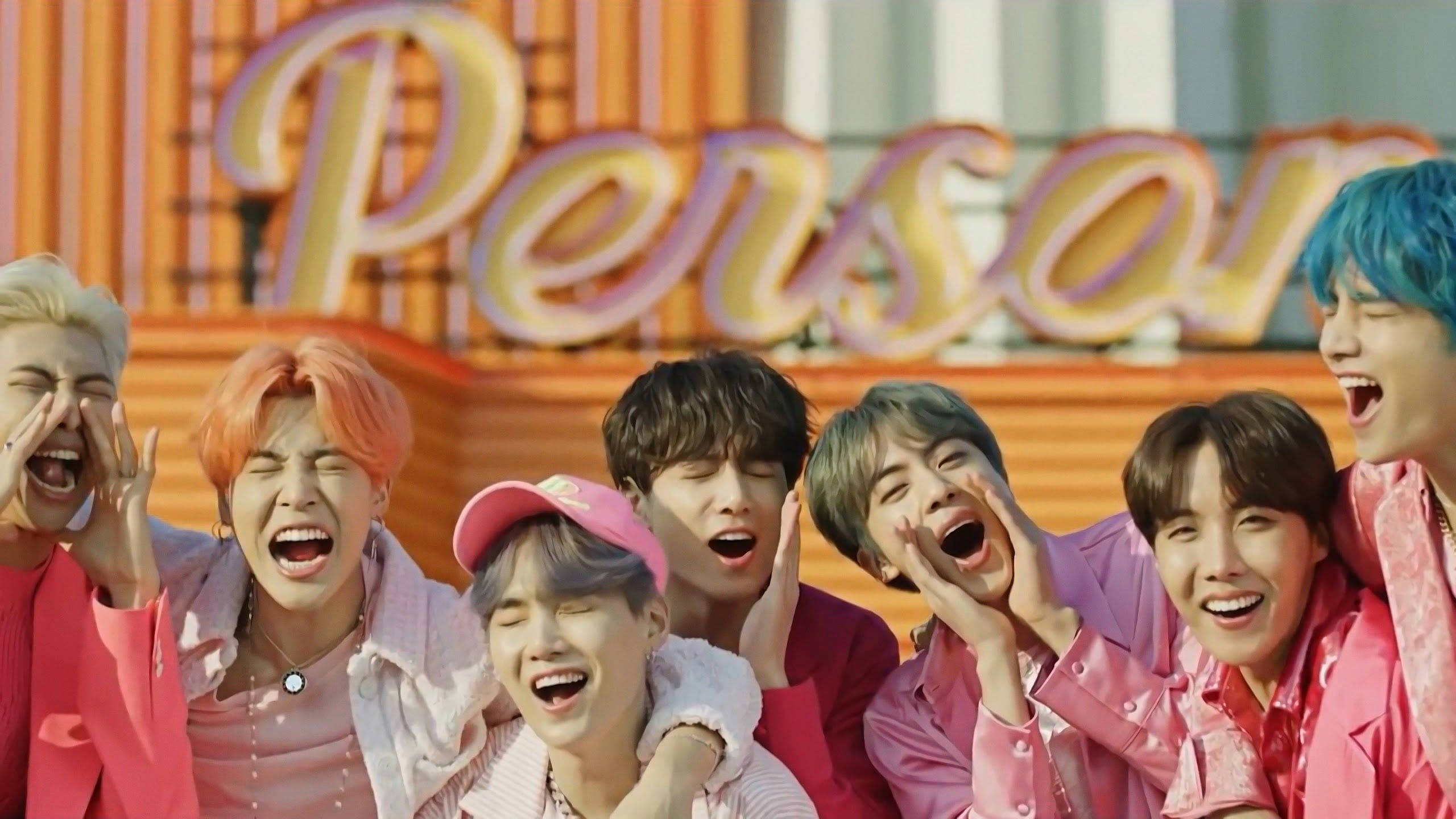 BTS 桌布 桌布 壁紙 — 七位擁有繽紛髮色的年輕男子在一個寫著「Person」的粉紅色大型霓虹燈牌前開懷大笑。