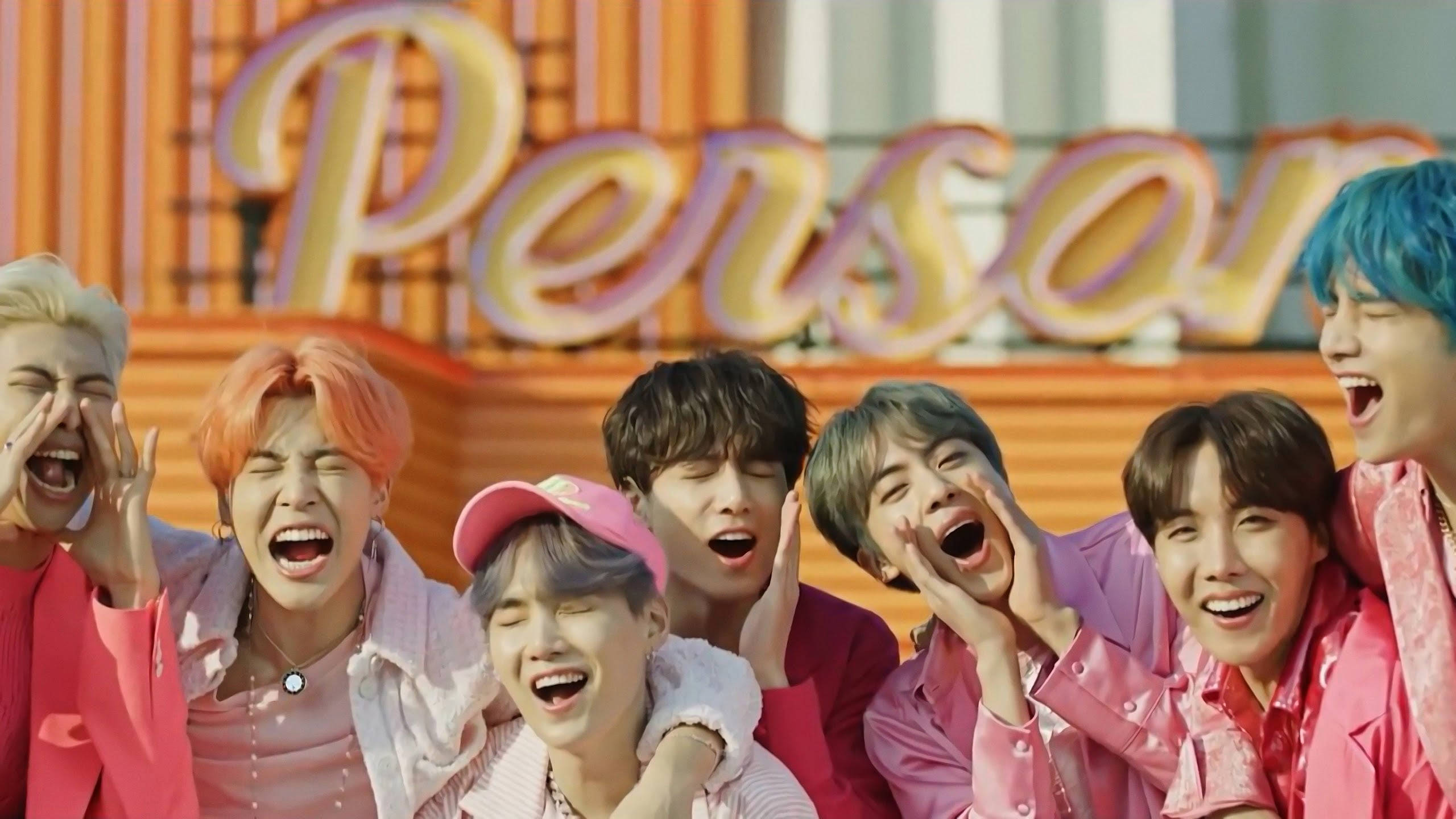 BTS 桌布 壁紙 — 七位擁有繽紛髮色的年輕男性在一個寫著「Person」的大型粉紅色霓虹燈牌前開懷大笑。