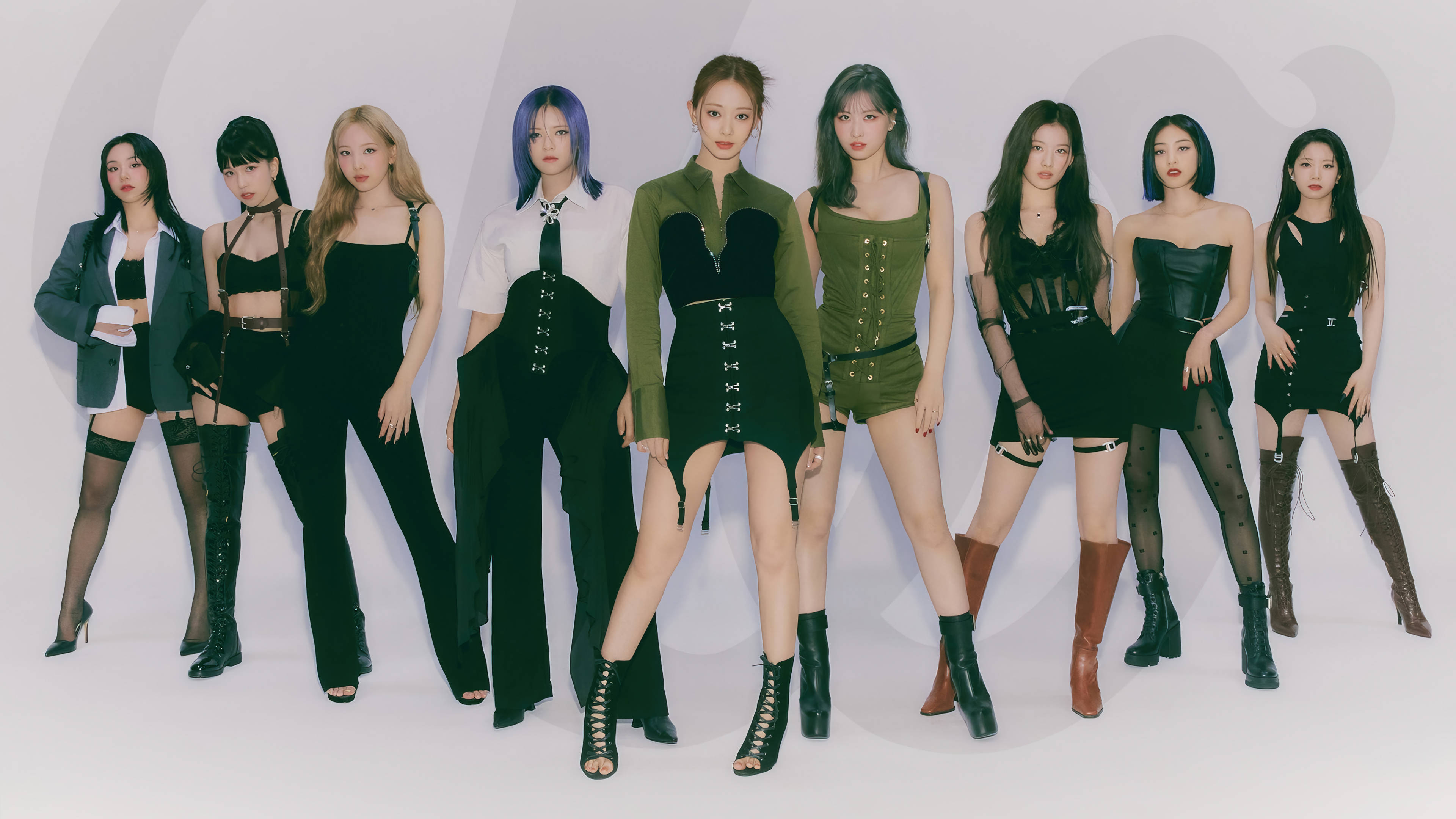 Kpop Aesthetic 桌布 壁紙 — 七位時尚女性穿著前衛的黑色和橄欖色服裝，在極簡的白色工作室背景前自信地擺姿勢。