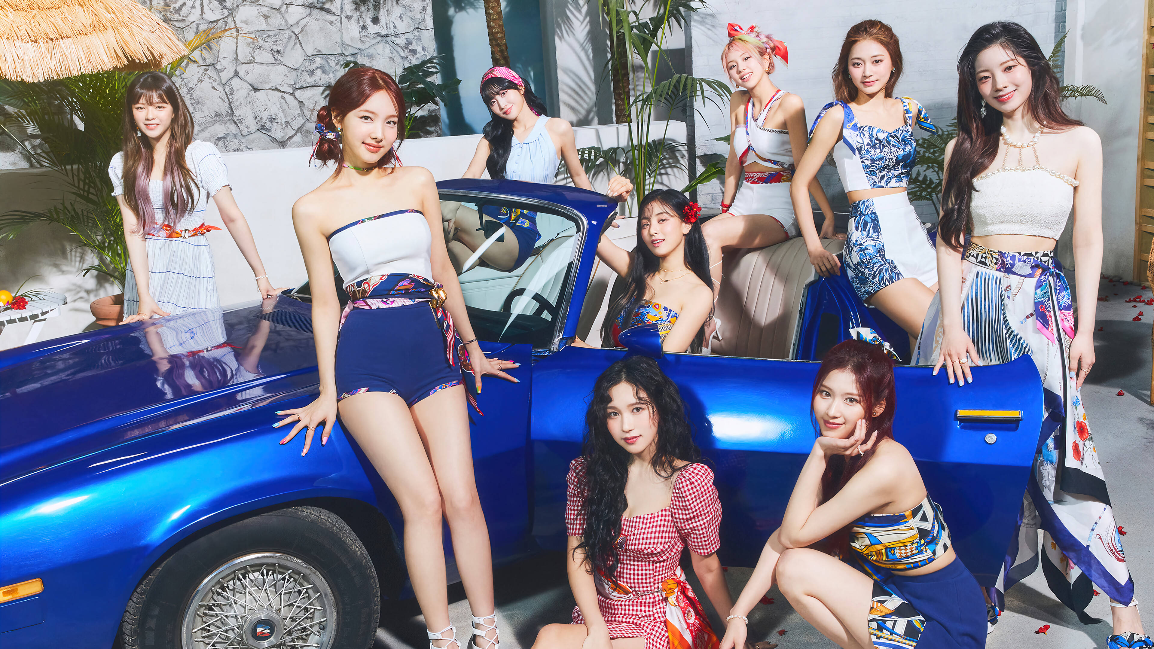 Kpop Aesthetic 桌布 壁紙 — 七位時尚女性穿著色彩繽紛的復古服裝，在熱帶庭院中圍著一輛閃亮的藍色敞篷車俏皮地擺姿勢。