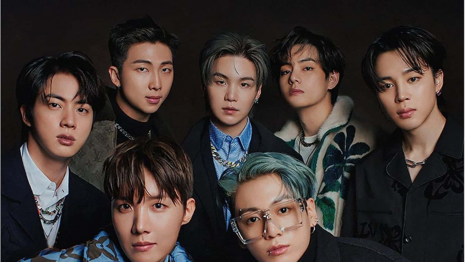 BTS 桌布 壁紙 — 七位時尚年輕男士，擁有不同髮色和現代服裝，在深色工作室背景下自信地擺姿勢。