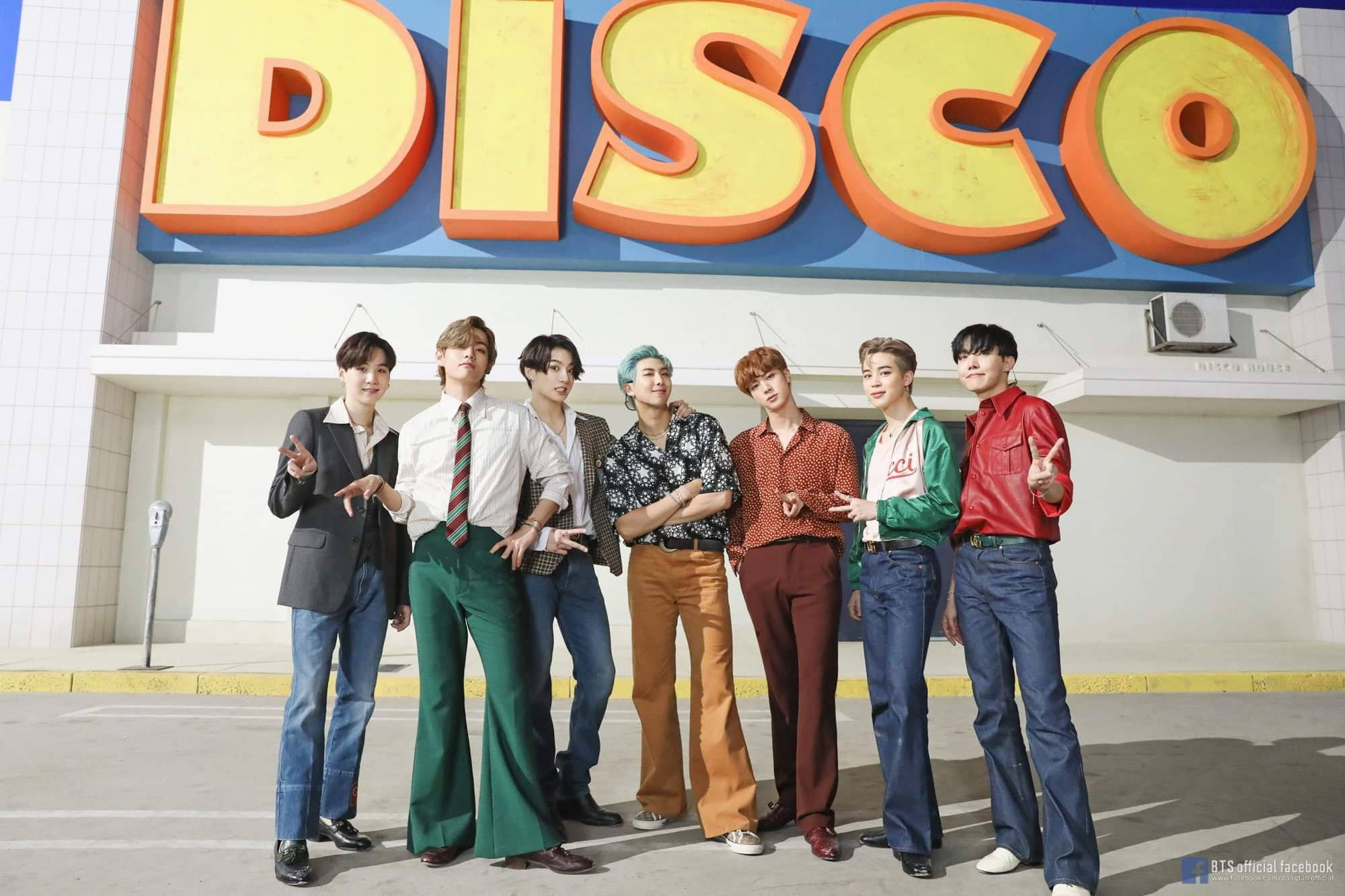 BTS 桌布 壁紙 — 七位時尚年輕男士在明亮的日光下，自信地站在一個巨大的復古黃橙色「DISCO」標誌前擺姿勢。