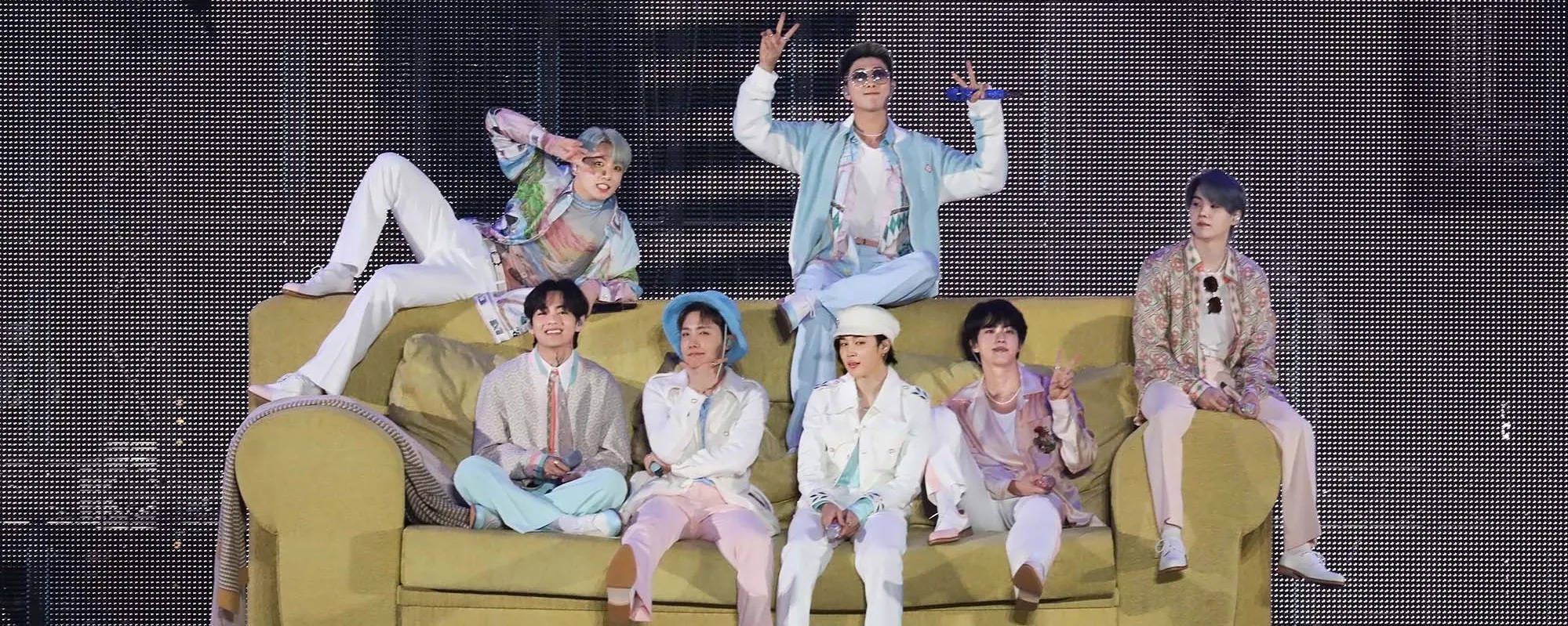 Bts Aesthetic 桌布 壁紙 — 七位時尚年輕男士在深色像素化舞台背景下，於一張黃色大沙發上擺出俏皮姿勢。