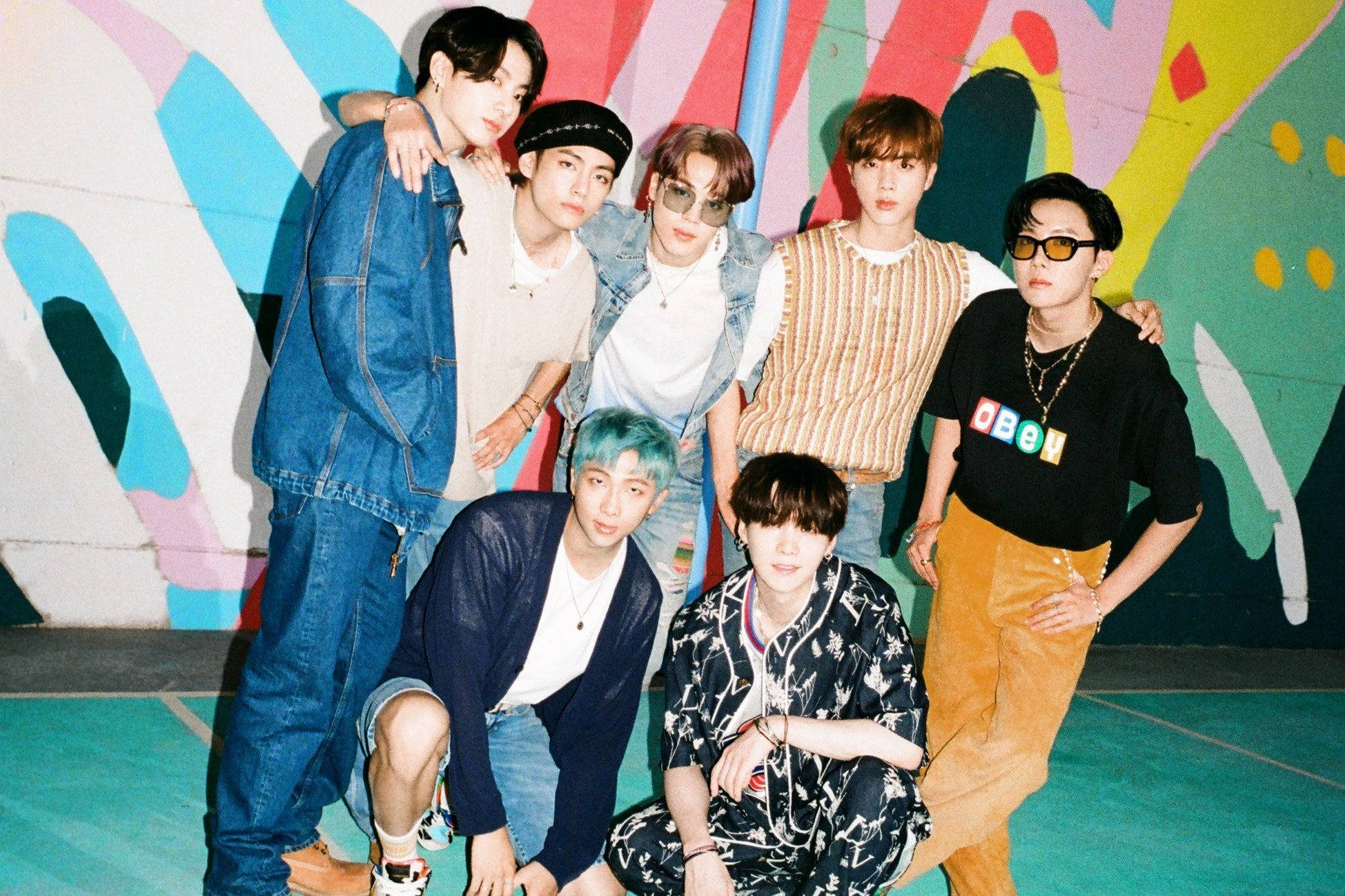 BTS 桌布 壁紙 — 七位時尚年輕男士在色彩繽紛的城市環境中，自信地站在充滿活力的塗鴉牆前擺姿勢。
