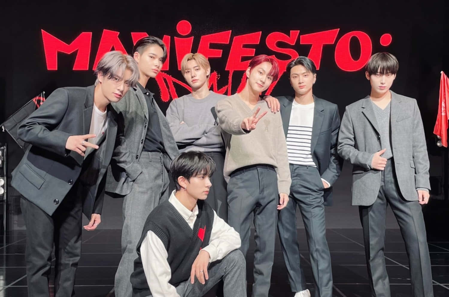 Enhypen Laptop 桌布 壁紙 — 七位時尚年輕男士在鮮紅色「MANIFESTO」背景下，自信地穿著灰色西裝和休閒服裝擺姿勢。