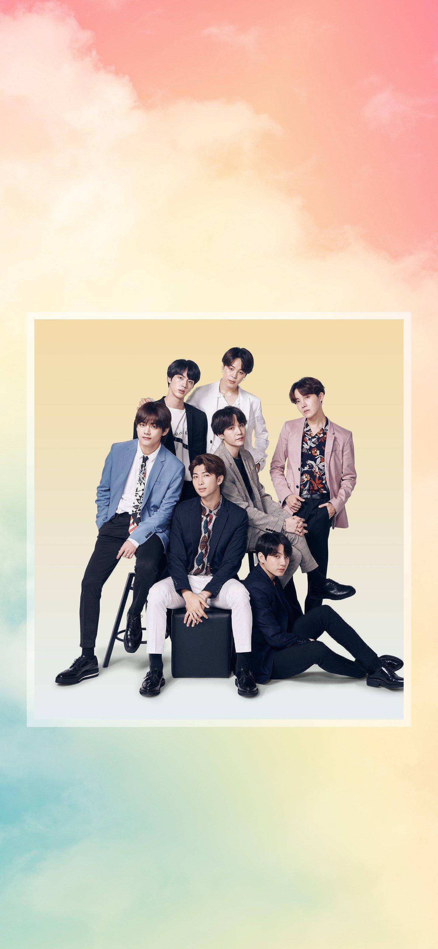 BTS 桌布 壁紙 — 七位時尚年輕男士穿著時尚西裝，在柔和粉彩漸變天空背景下自信地擺姿勢。