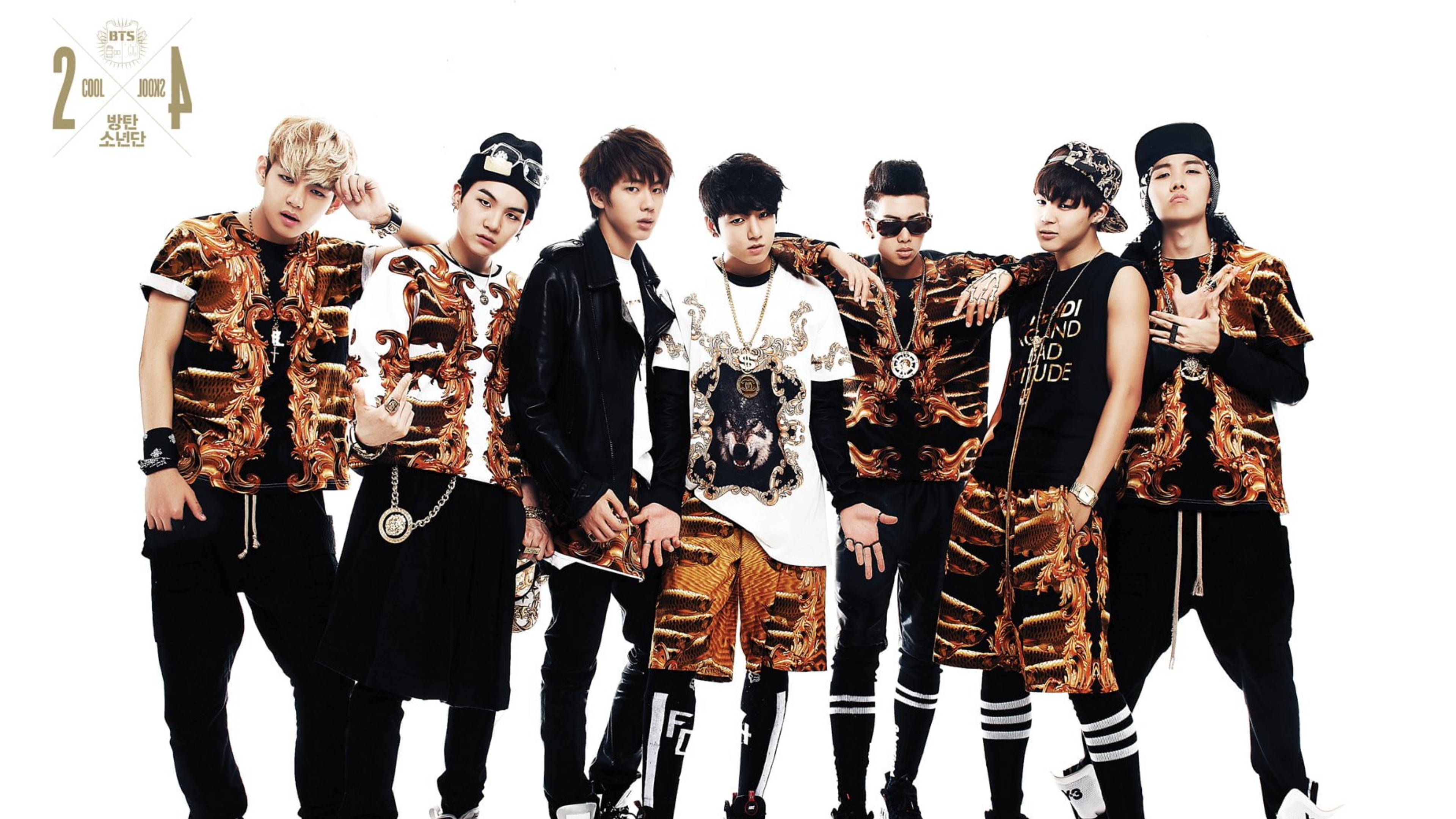 BTS 桌布 壁紙 — 七位時尚年輕男士身穿大膽的金色和黑色圖案服裝，在純白背景前自信地擺姿勢。