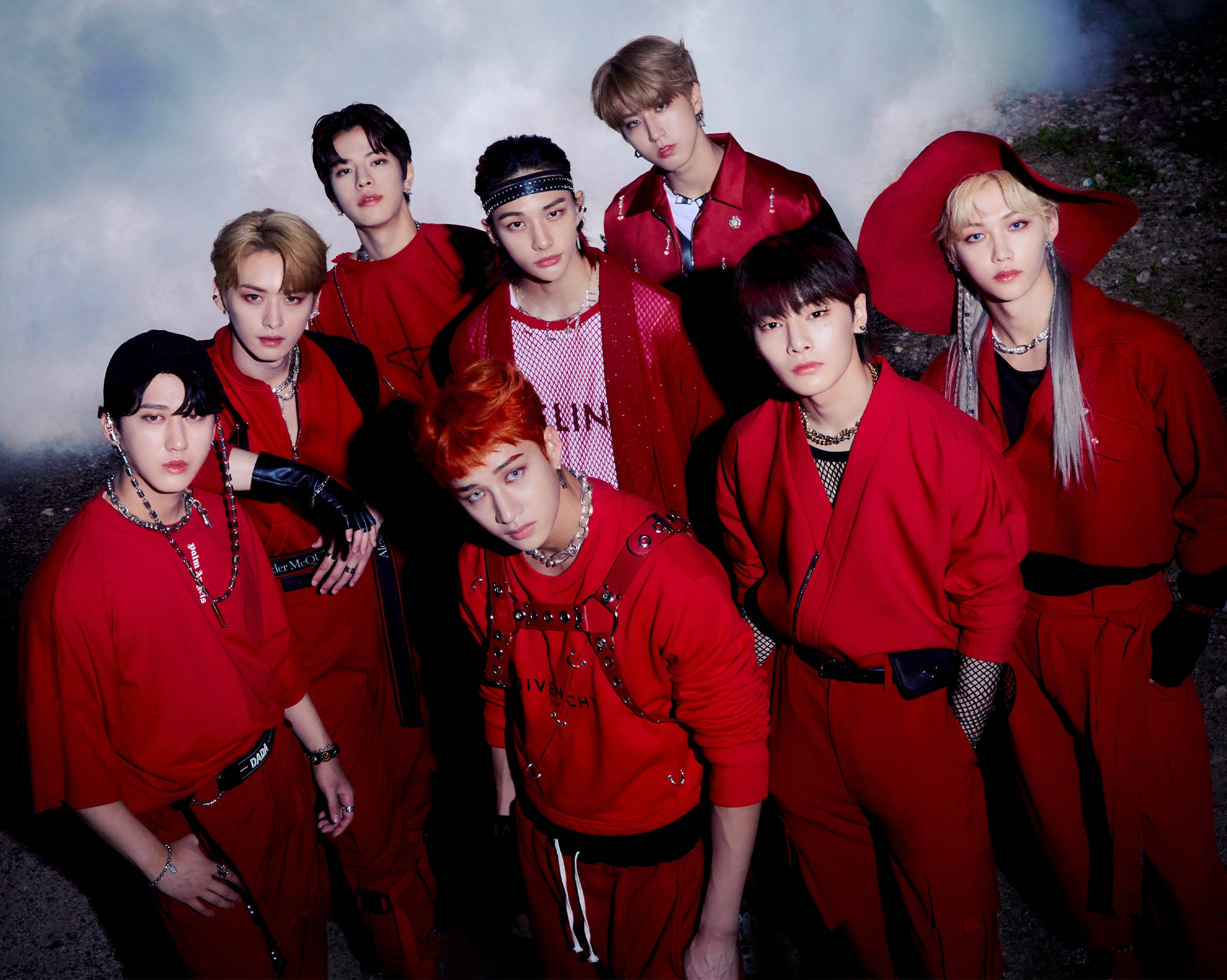 Stray Kids 桌布 壁紙 — 七位時尚年輕男士身穿大膽紅色服裝，在陰雲密佈的背景和戲劇性燈光下自信地擺姿勢。